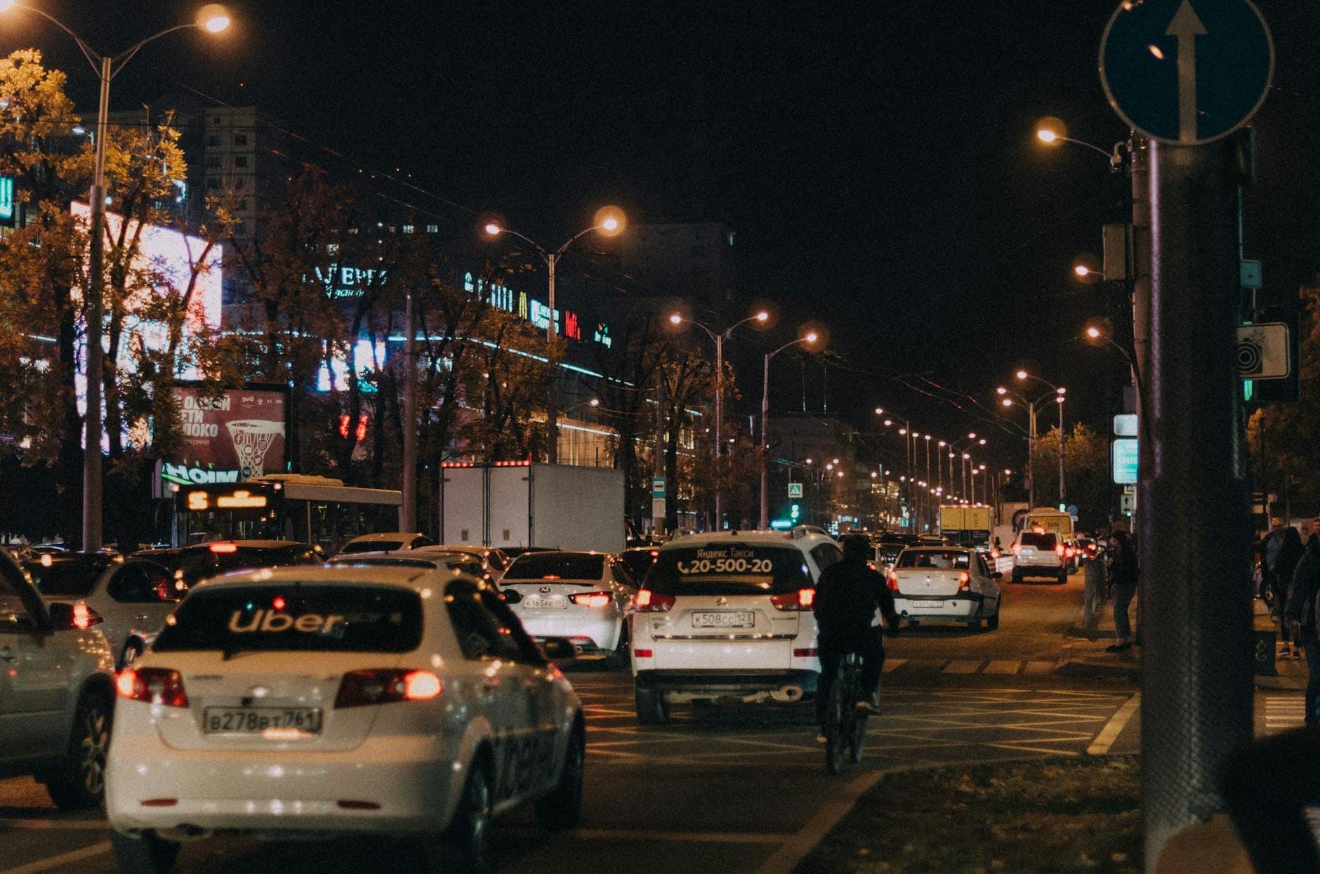 Movimentada rua da Cidade do México à noite com carros, incluindo um Uber, pessoas e luzes da cidade, ilustrando o transporte noturno urbano.