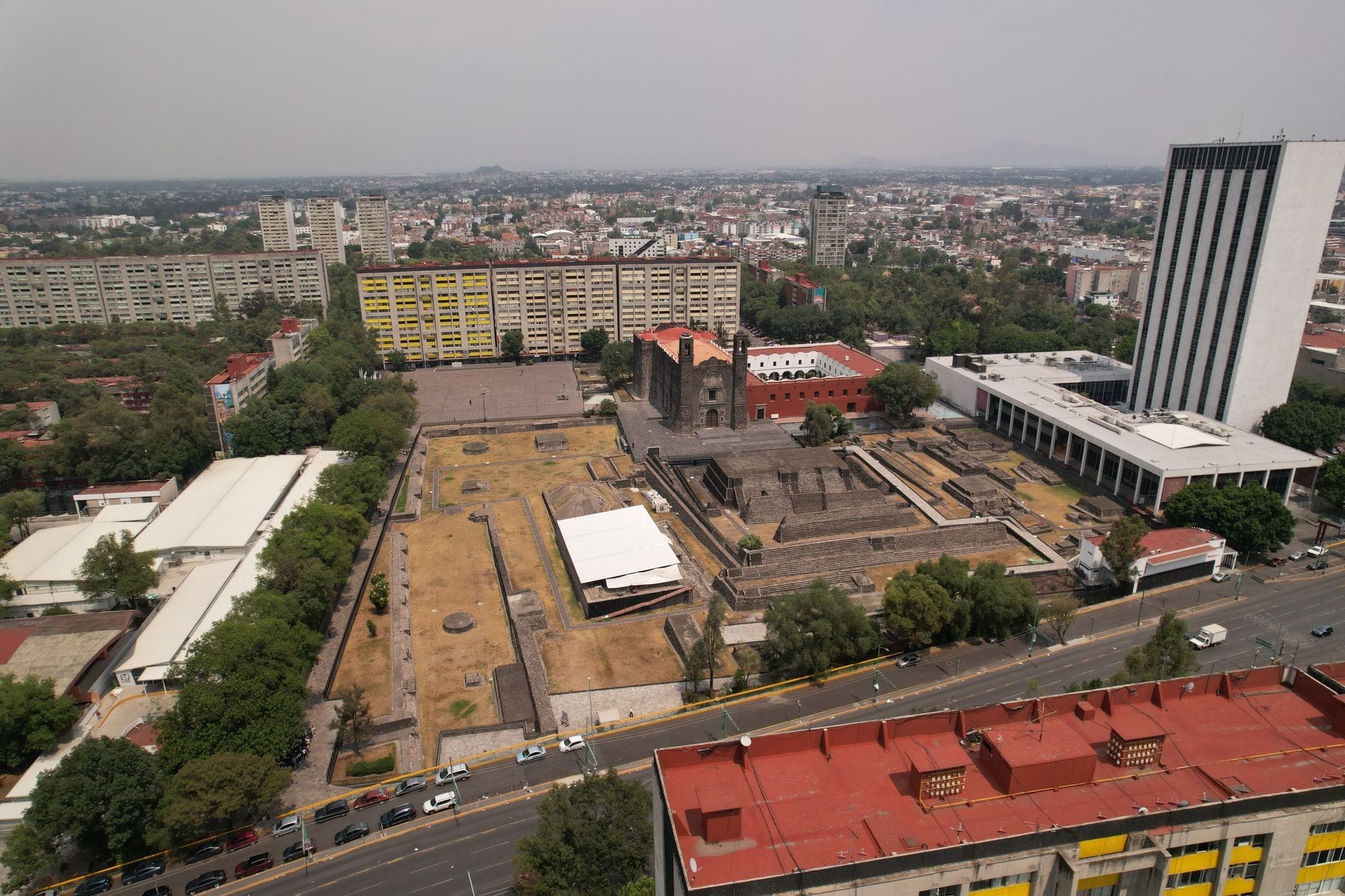 Vue aérienne du site archéologique de Tlatelolco à Mexico, avec des ruines anciennes, une église coloniale et des bâtiments modernes à proximité.
