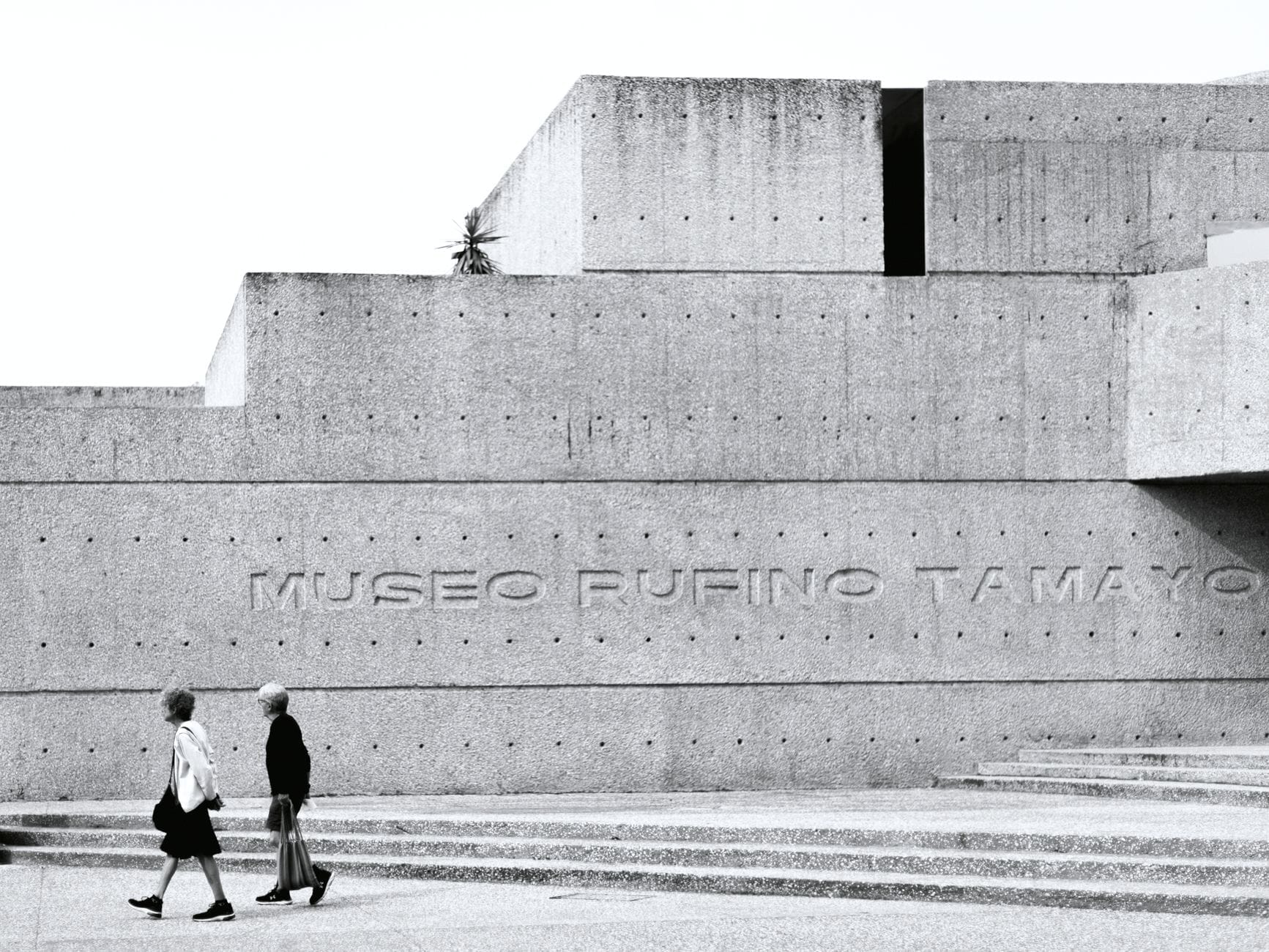 Façade moderne en béton du Museo Rufino Tamayo avec deux personnes marchant devant, mettant en valeur l'extérieur d'un musée bien connu de Mexico.