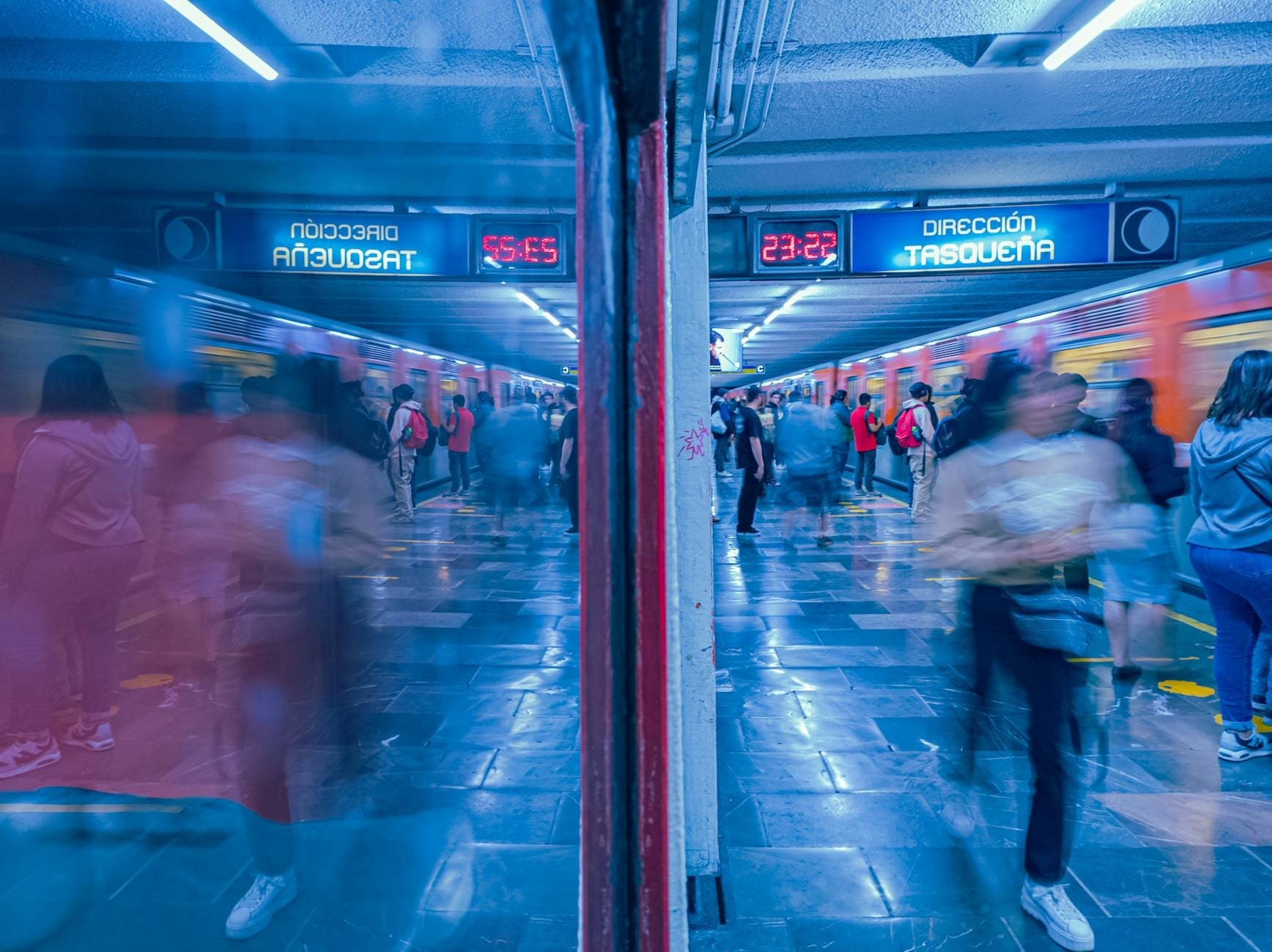 Plataforma movimentada do Metro da Cidade do México com passageiros e painéis digitais de direção sobre os trilhos.