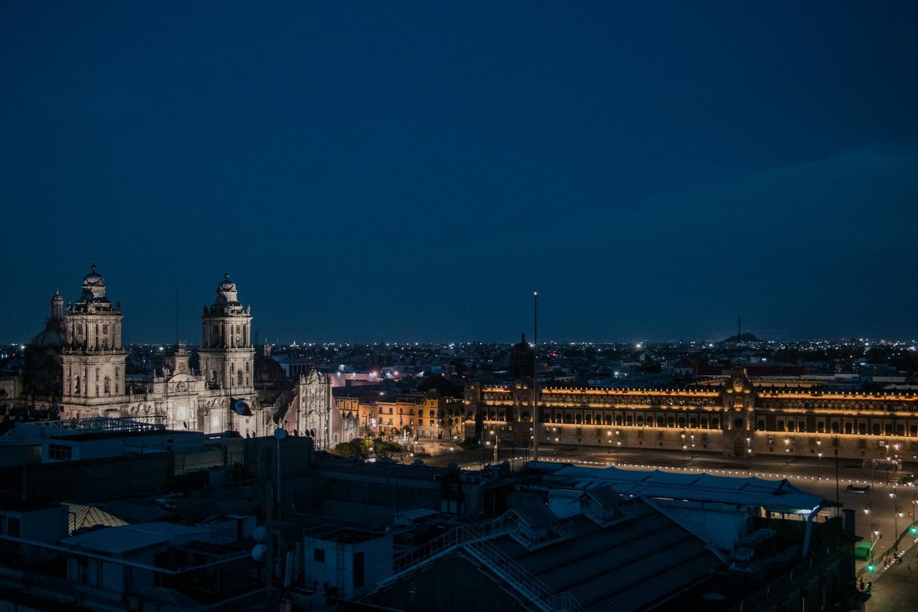 Vista aérea noturna do centro histórico da Cidade do México mostrando a Catedral Metropolitana e o Zócalo iluminado.