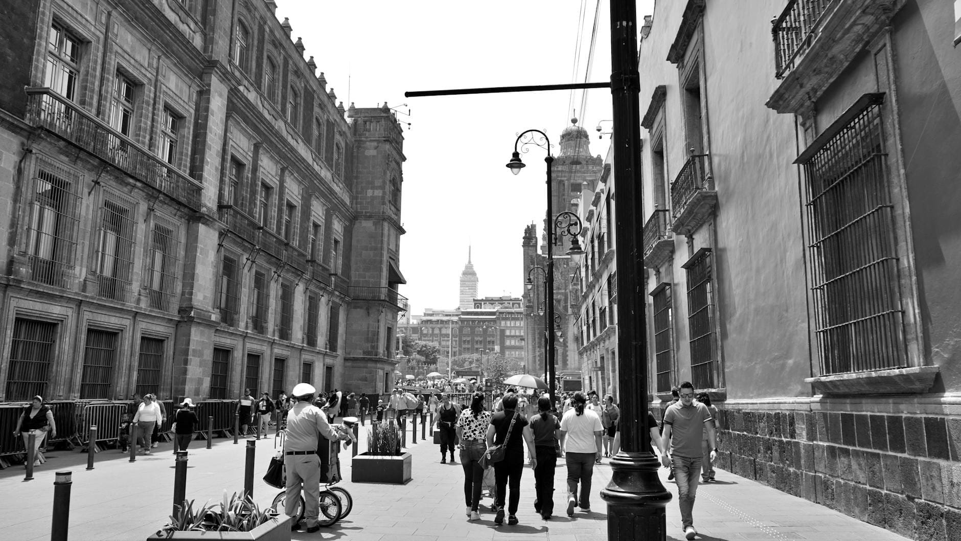 Rua de pedestres na Cidade do México com pessoas caminhando, cercada por históricos edifícios coloniais e a Torre Latinoamericana ao fundo.