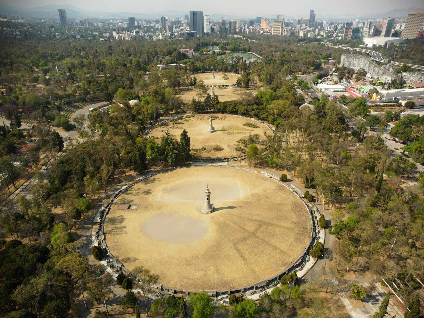 Vista aérea do Parque Chapultepec com amplos caminhos, áreas verdes abertas e o horizonte da cidade em um dia claro na Cidade do México.