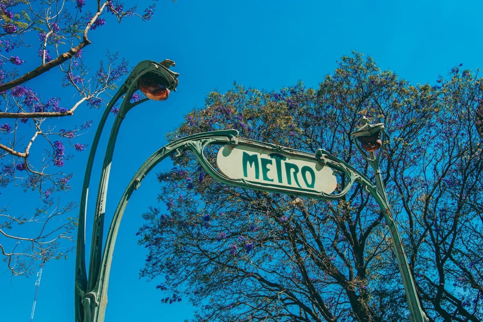 Placa de entrada do metrô Art Nouveau na Cidade do México cercada por árvores e céu azul limpo.