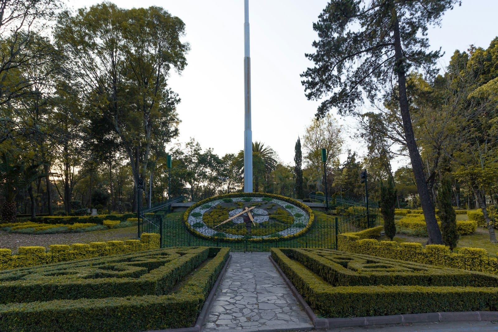 Grande relógio floral e jardins bem cuidados no Parque Chapultepec, rodeados por árvores altas em um dia ensolarado.