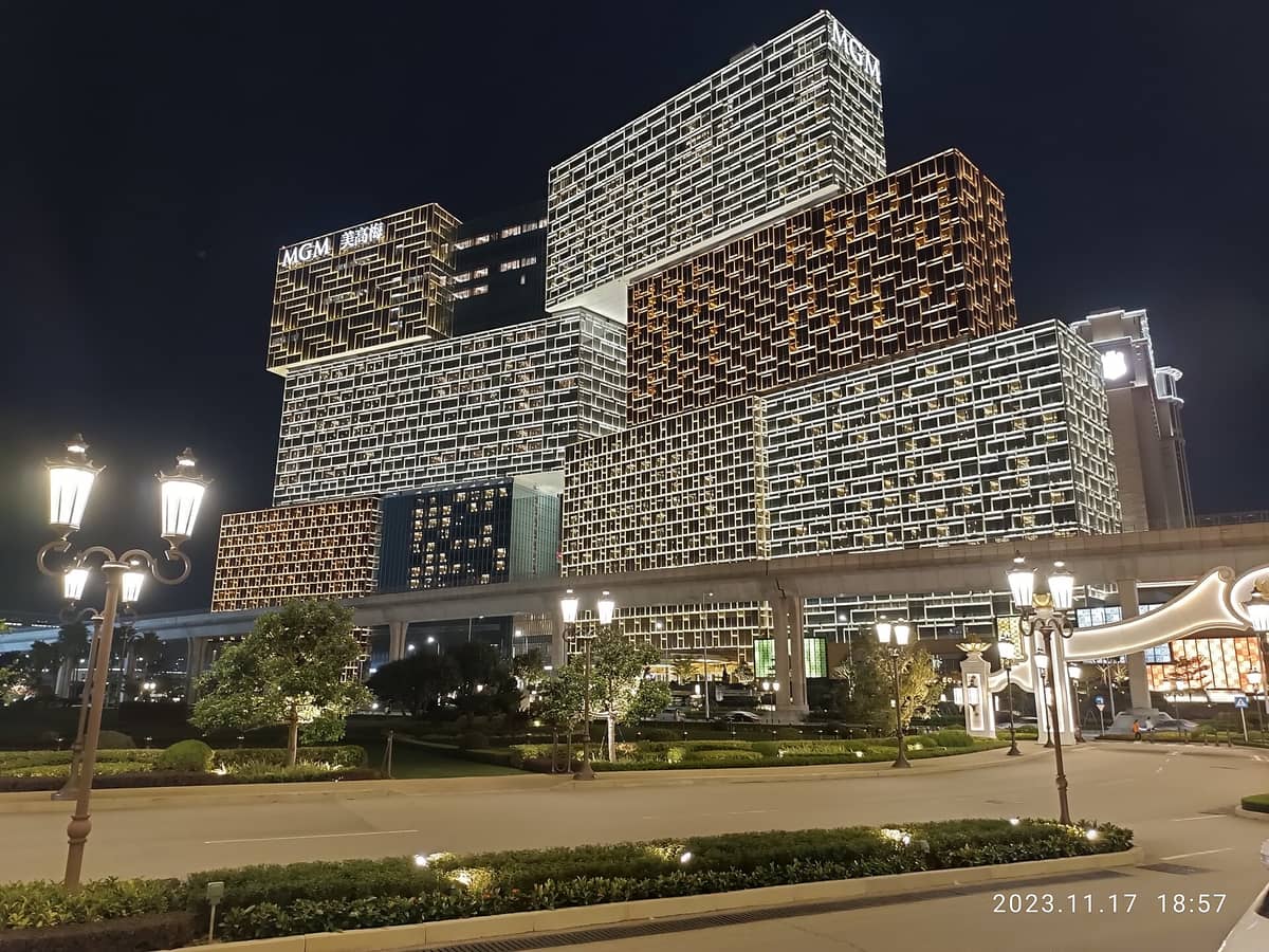 Nächtliche Ansicht der markanten gestapelten Glasfassade des MGM Cotai in stimmungsvoller Beleuchtung, mit umliegenden Gartenanlagen und Straßenlaternen am Eingang am Cotai Strip in Macau.