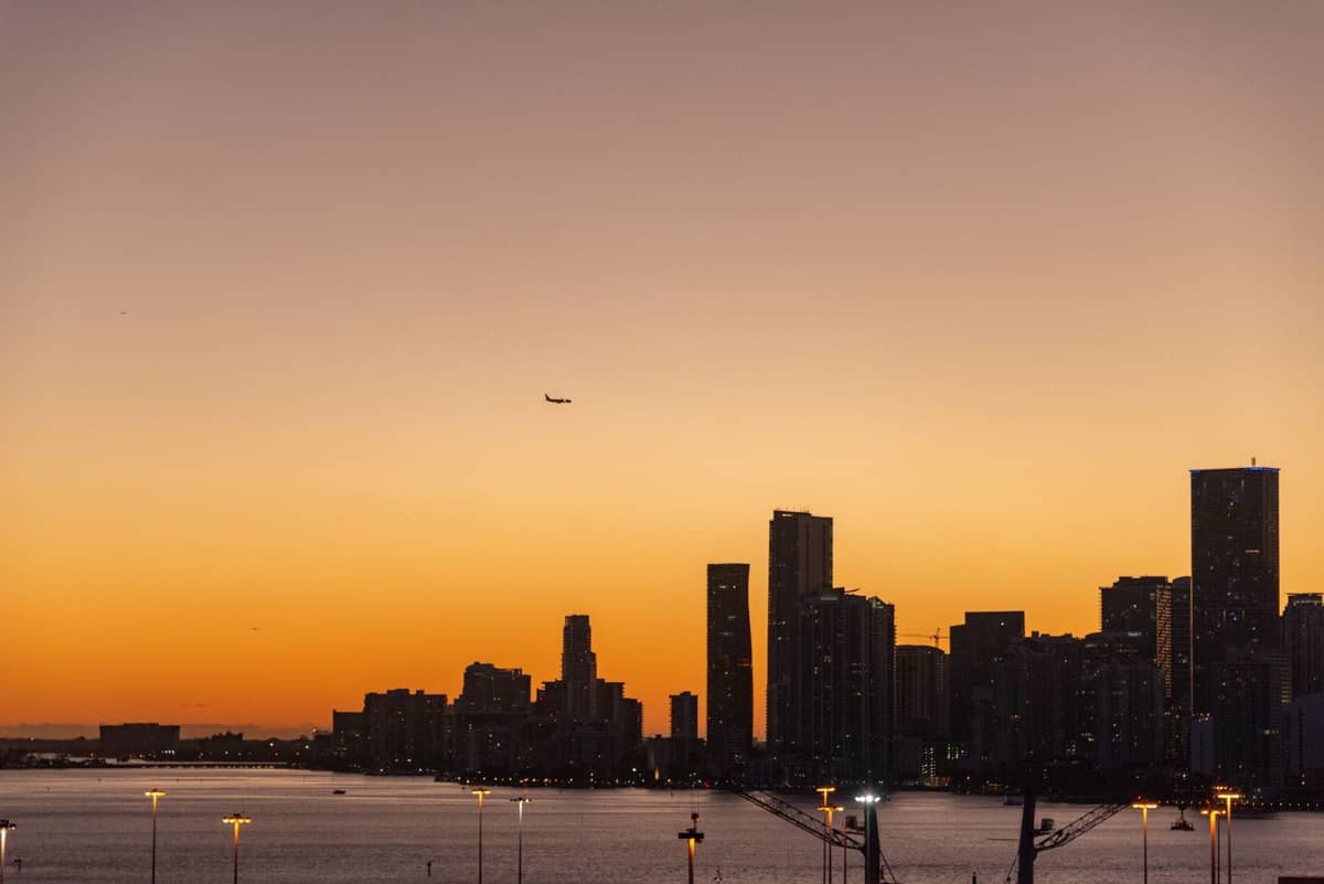 Miami skyline at sunset with a plane approaching above the city and water in the foreground