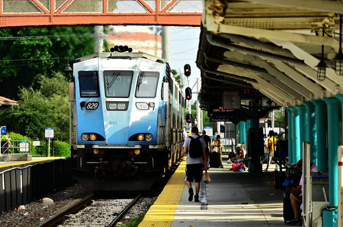 Tri-Rail commuter train arriving at an outdoor station platform with passengers waiting, a common ground transportation option in Miami.