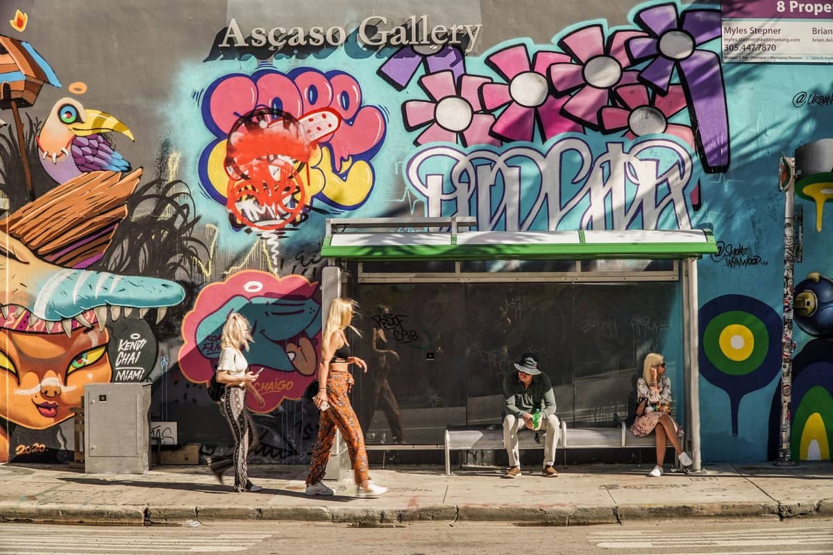People walking and sitting in front of colorful street art murals at Ascaso Gallery during daylight in Miami’s Wynwood Arts District.