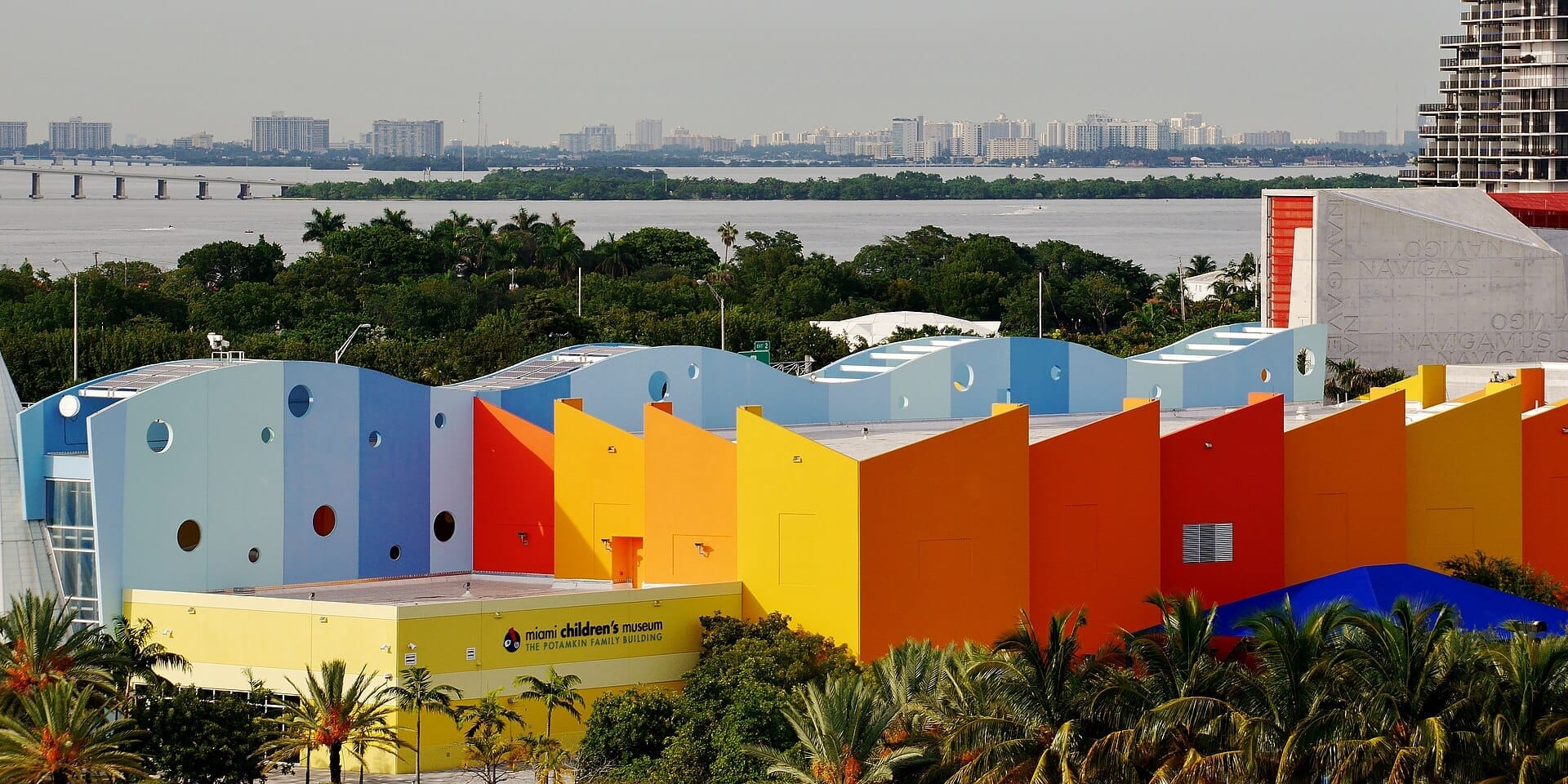 Vista esterna del Miami Children's Museum con facciate geometriche colorate, palme e la baia di Biscayne con lo skyline di Miami sullo sfondo.