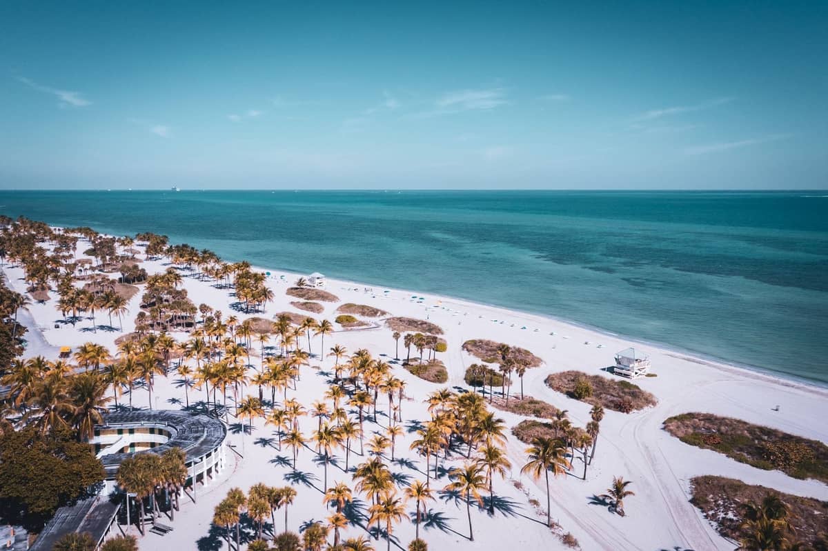 Aerial view of a quiet white sand beach lined with palm trees and surrounded by clear turquoise waters in Miami.