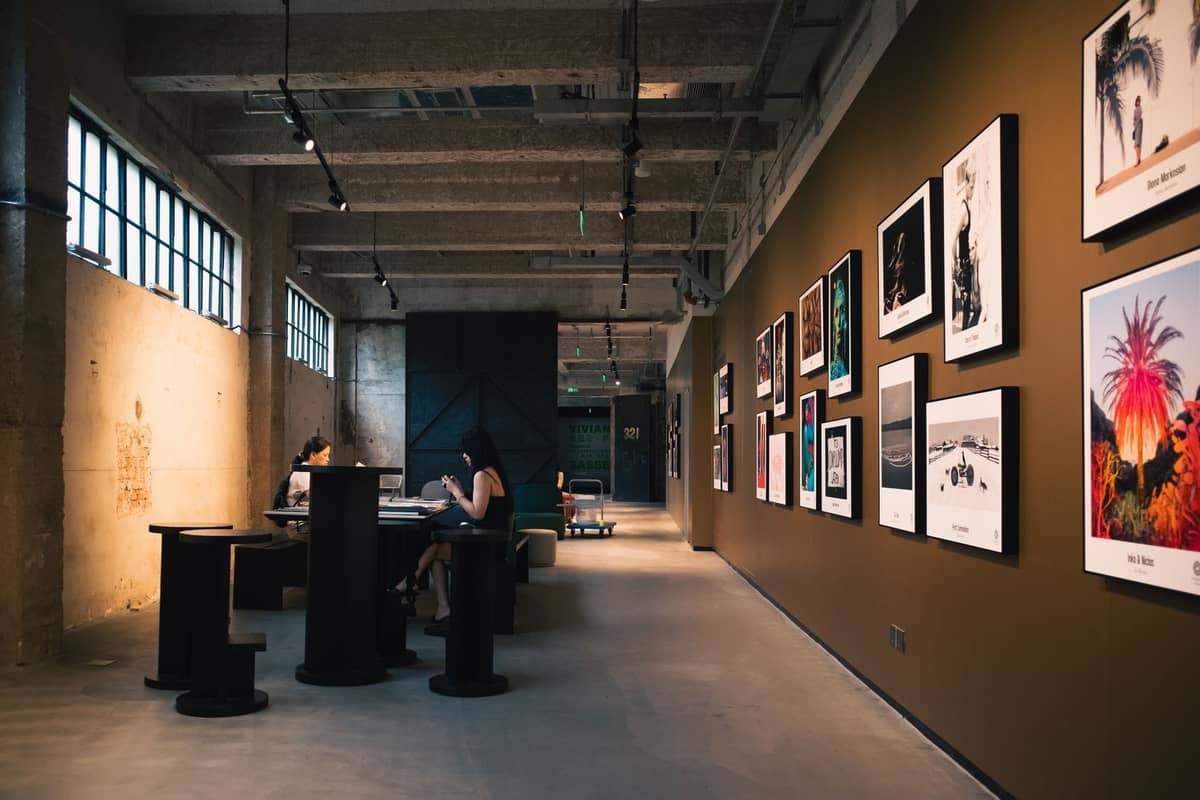 Contemporary art gallery with framed photographs and visitors, concrete and industrial design, warm lighting, and creative ambiance.