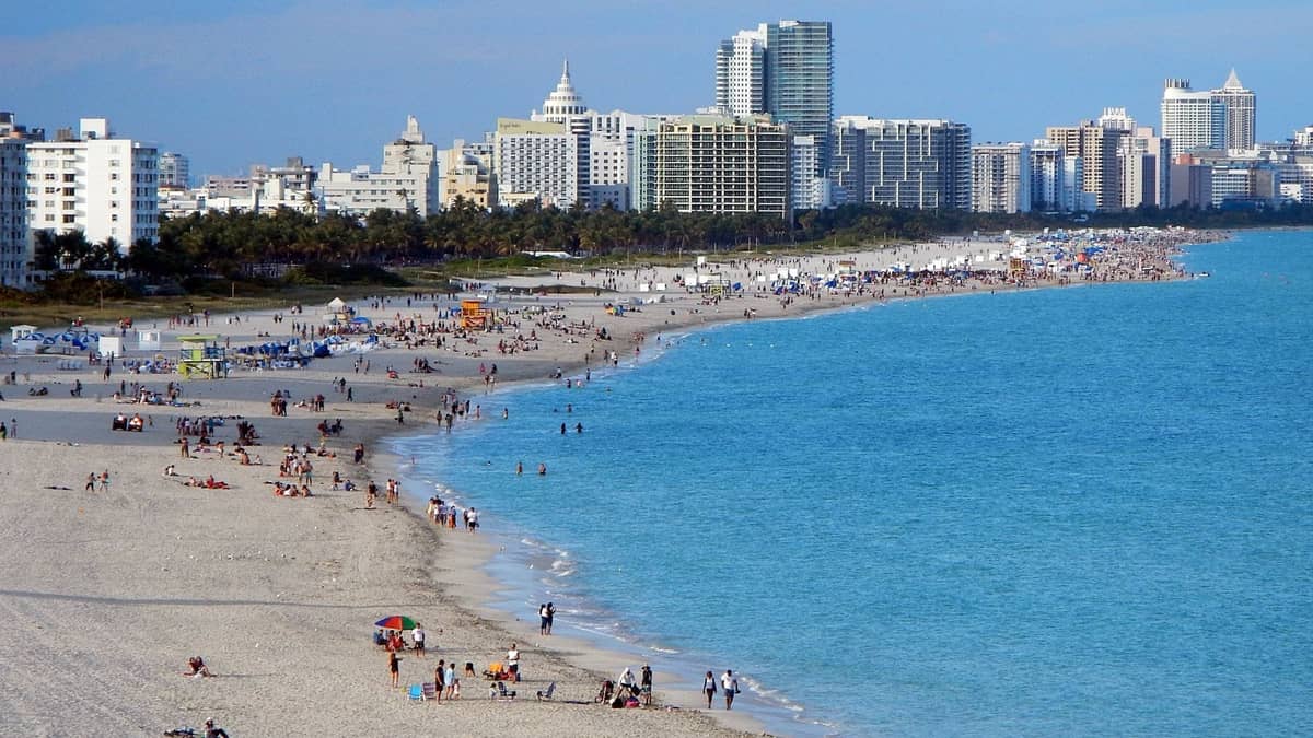 Wide view of Miami Beach with people enjoying the shore and city skyline visible in the background on a sunny day.
