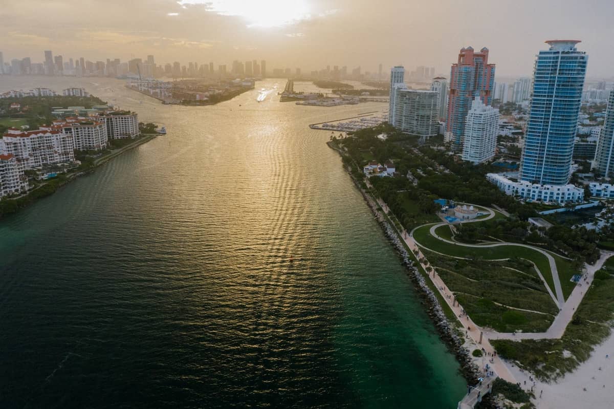 Aerial view of Miami luxury waterfront high-rises and upscale neighborhoods at sunset with water and city skyline in the background.