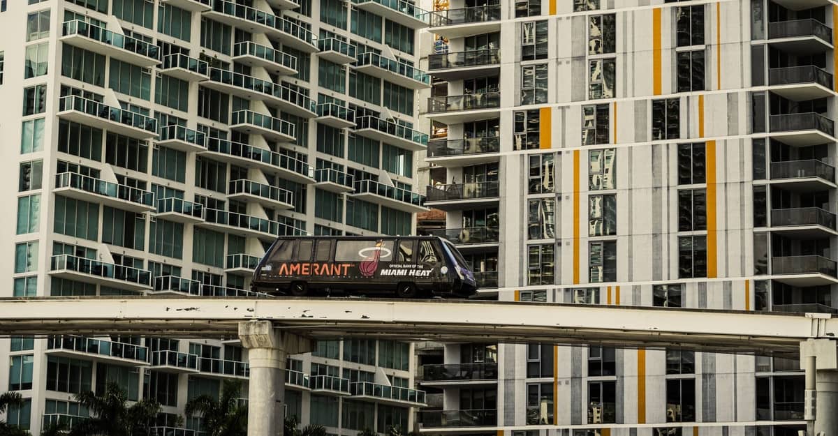 The Miami Metromover glides on elevated tracks in downtown with high-rise condos in the background.