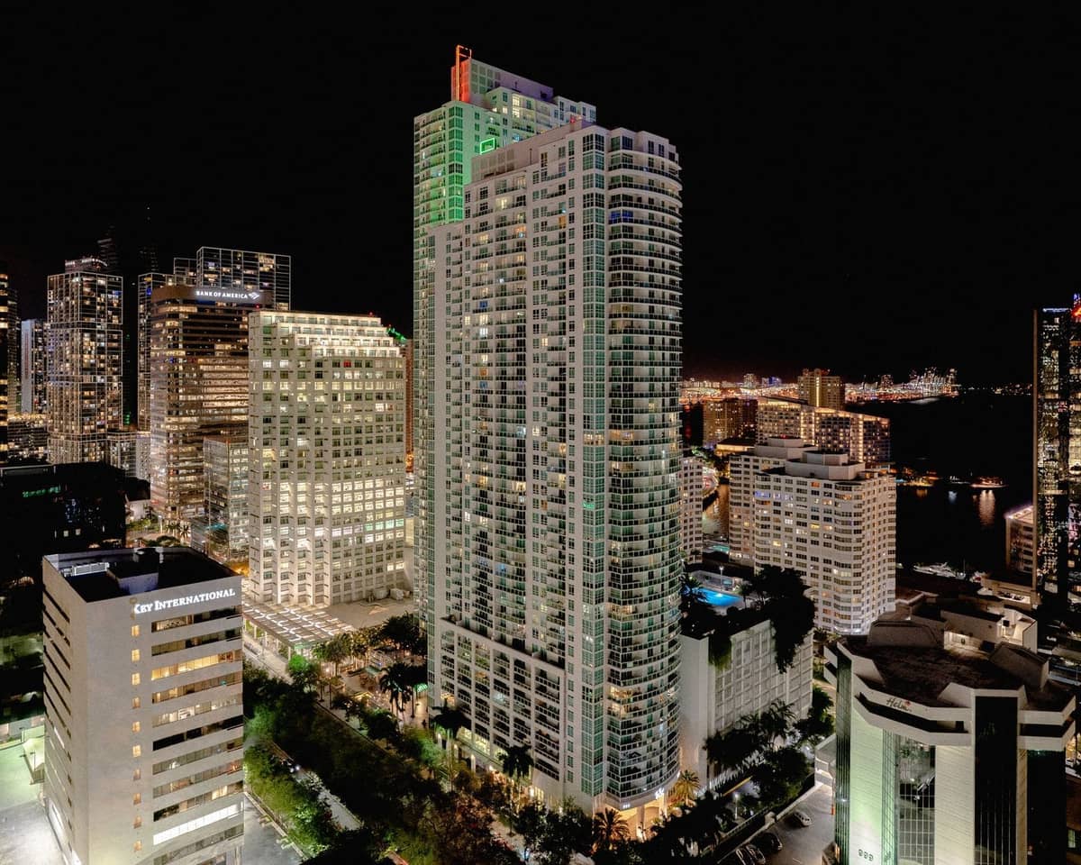 Nighttime view of downtown Miami with high-rise hotels and condominiums brightly lit, showing the urban Brickell area where many festival attendees stay.
