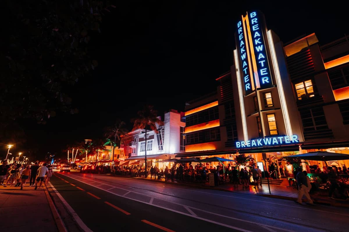 Bustling Miami nightlife scene on Ocean Drive with neon-lit Art Deco buildings, crowds of people, and vibrant club atmosphere at night.