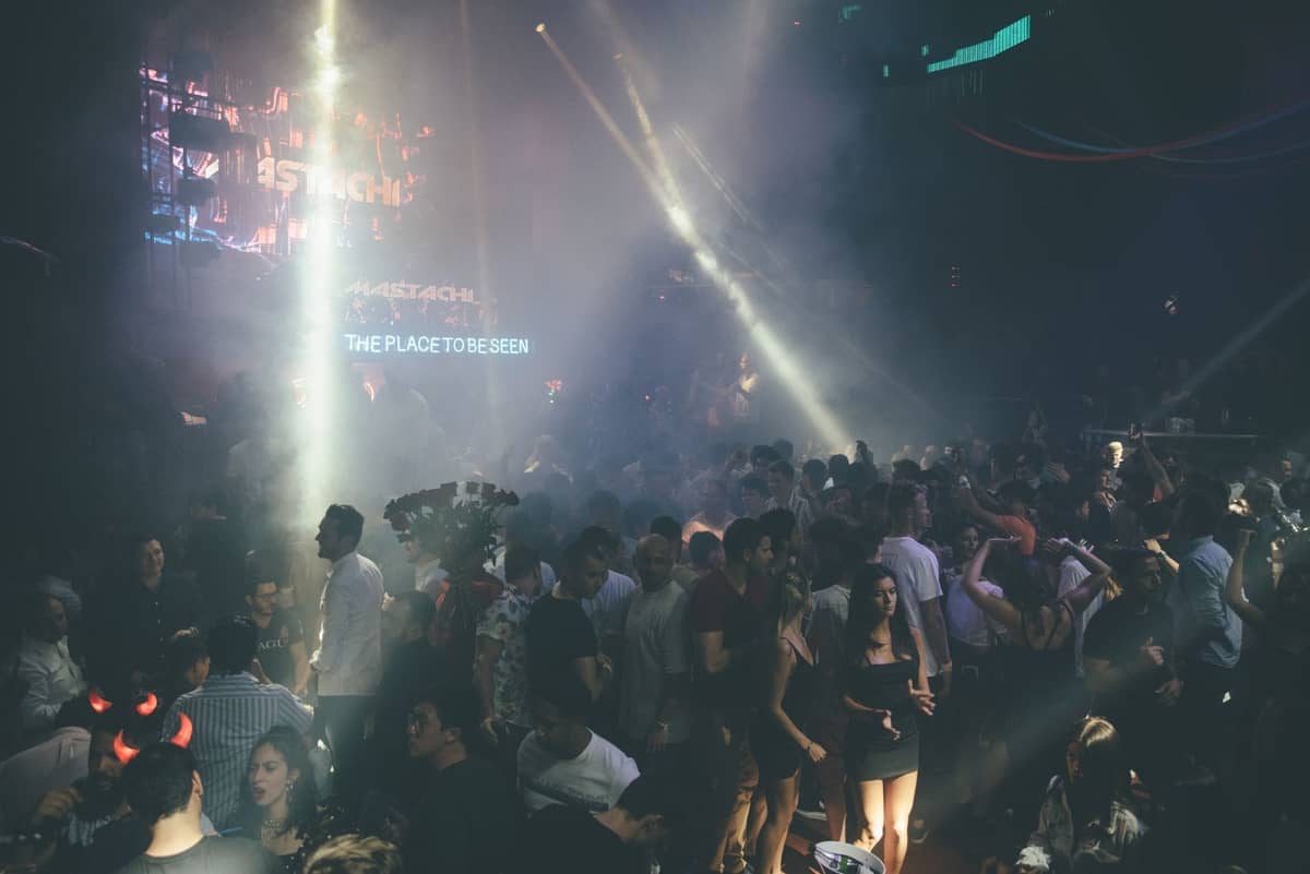Large crowd dancing and mingling in a packed nightclub with spotlights and screens, capturing Miami nightlife energy.