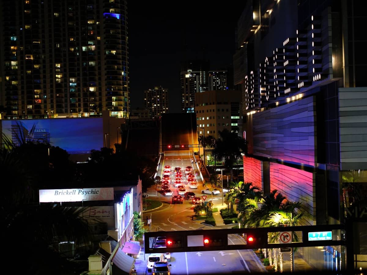 Night view of Miami's Brickell area with traffic, illuminated high-rise buildings, palm trees, and city lights. A typical urban scene reflecting downtown nightlife.