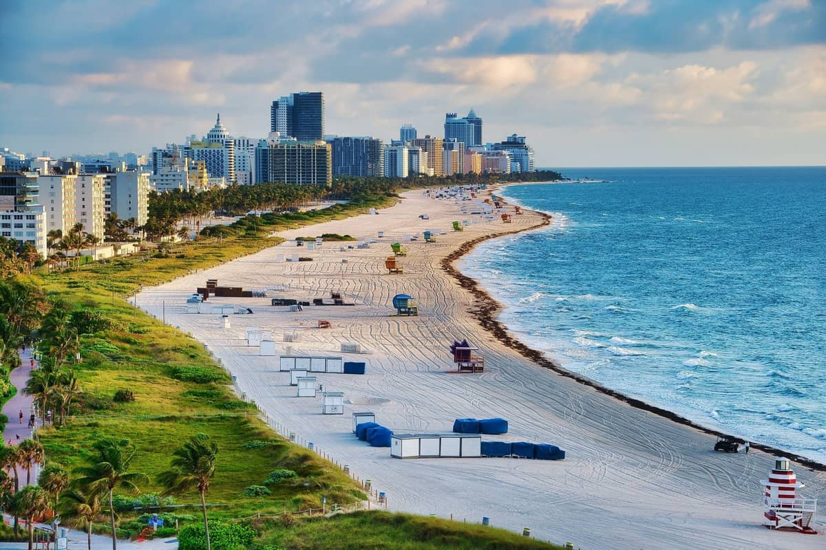Wide view of South Beach in Miami with colorful lifeguard stands, city buildings, and the ocean stretching along white sandy shore.