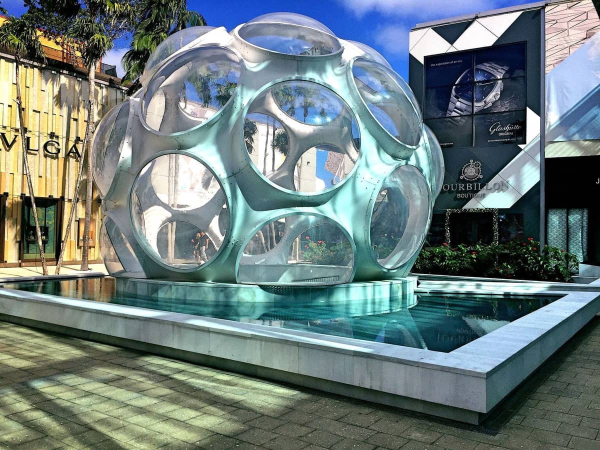Outdoor scene in Miami Design District showing the iconic Buckminster Fuller Fly's Eye Dome surrounded by luxury boutiques and palm trees.