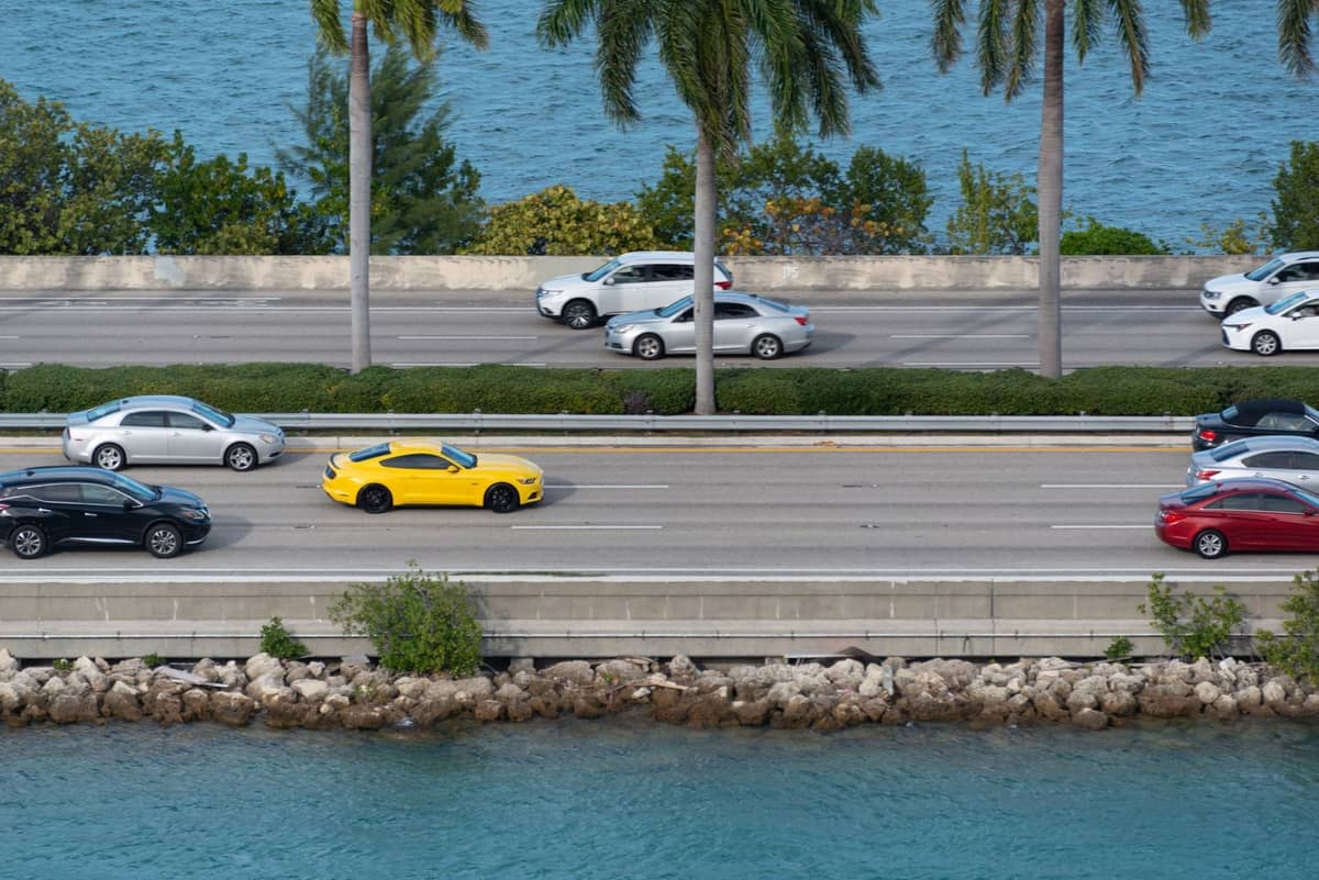 Overhead view of a Miami highway running alongside blue water with palm trees and cars driving in both directions.