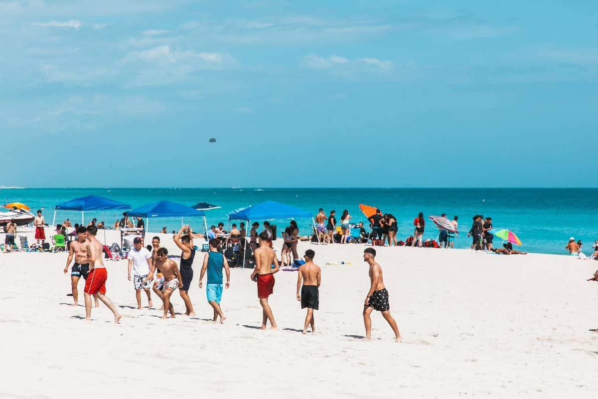 Crowded Miami beach scene with people playing and relaxing, umbrellas, turquoise water, and blue sky, illustrating different crowd levels.