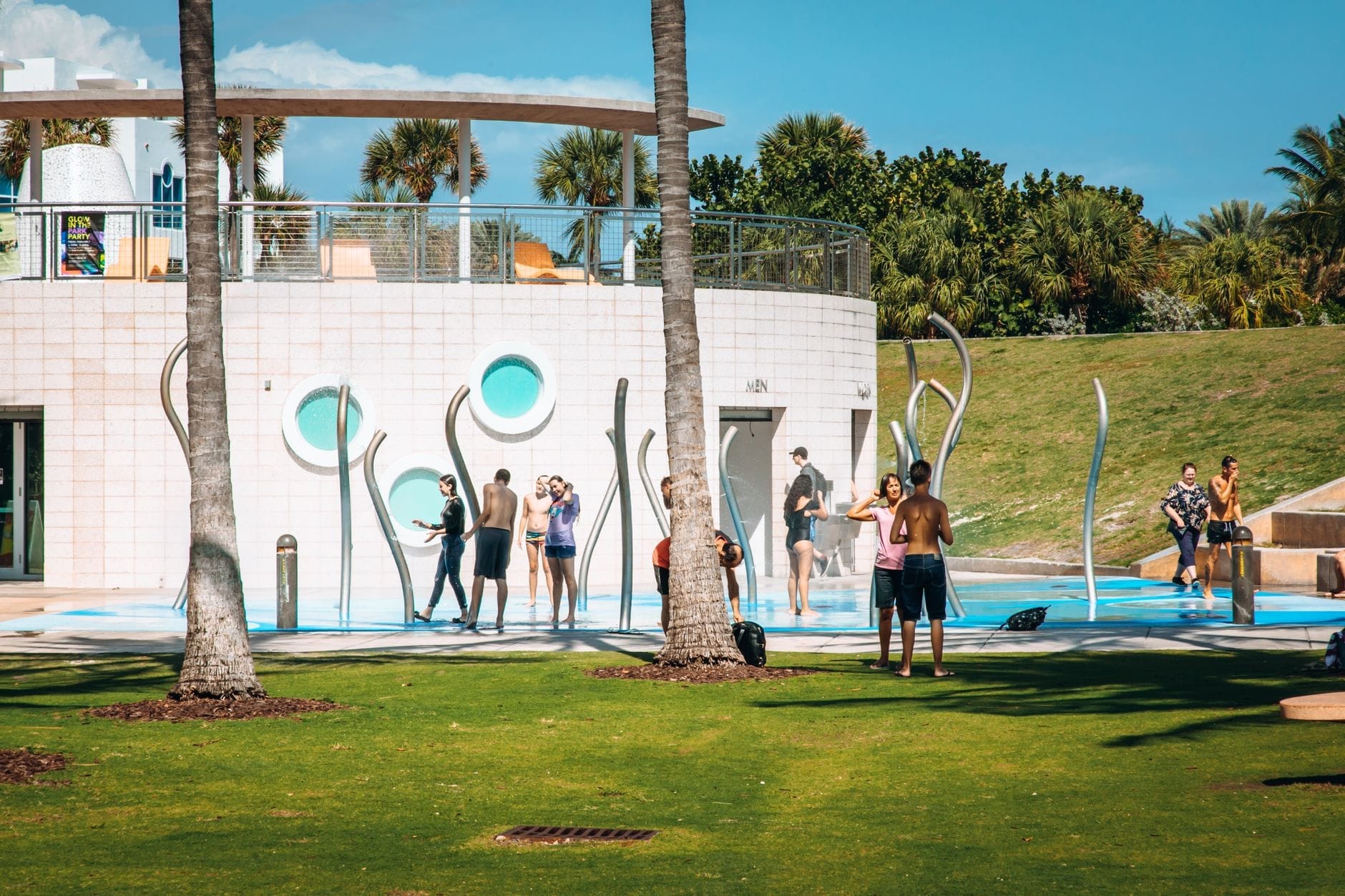 Crianças e famílias brincam em um espaço de água colorido cercado de palmeiras num ensolarado parque de Miami, perfeito para crianças e famílias.