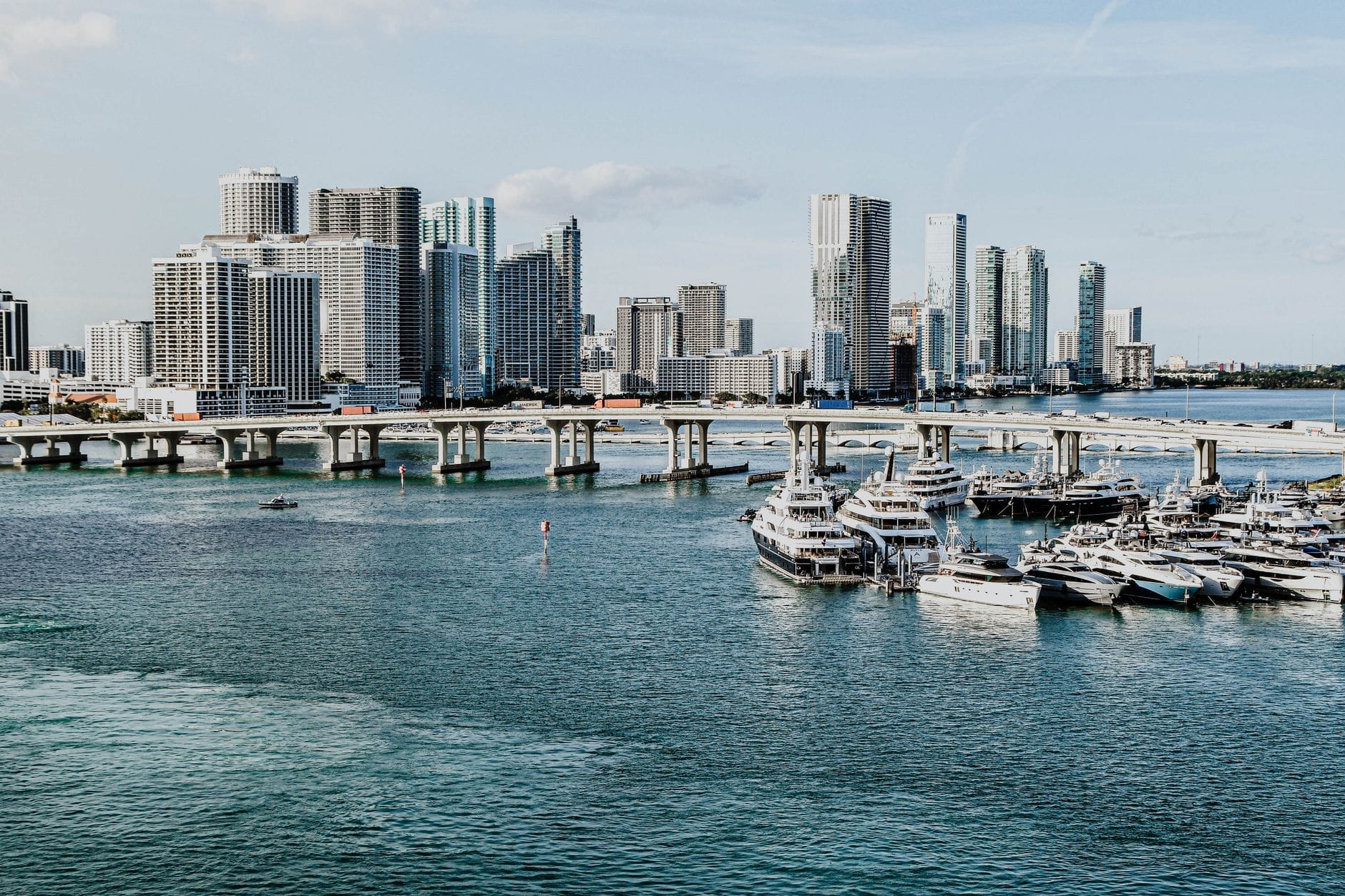 Vista panorâmica da marina de Miami com dezenas de iates e barcos atracados, tendo ao fundo o skyline moderno da cidade sob um céu limpo.