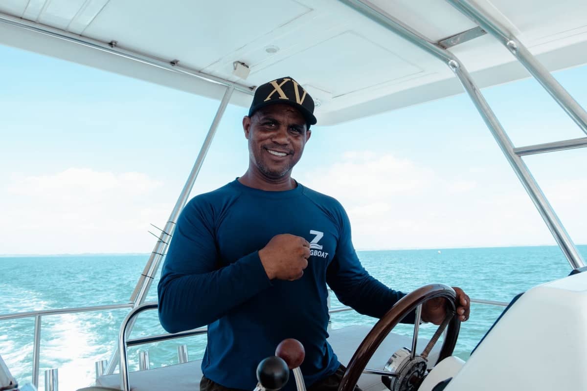 Smiling captain at the helm of a boat with open sea and Miami-style skyline in the background, exemplifying a captained charter option.