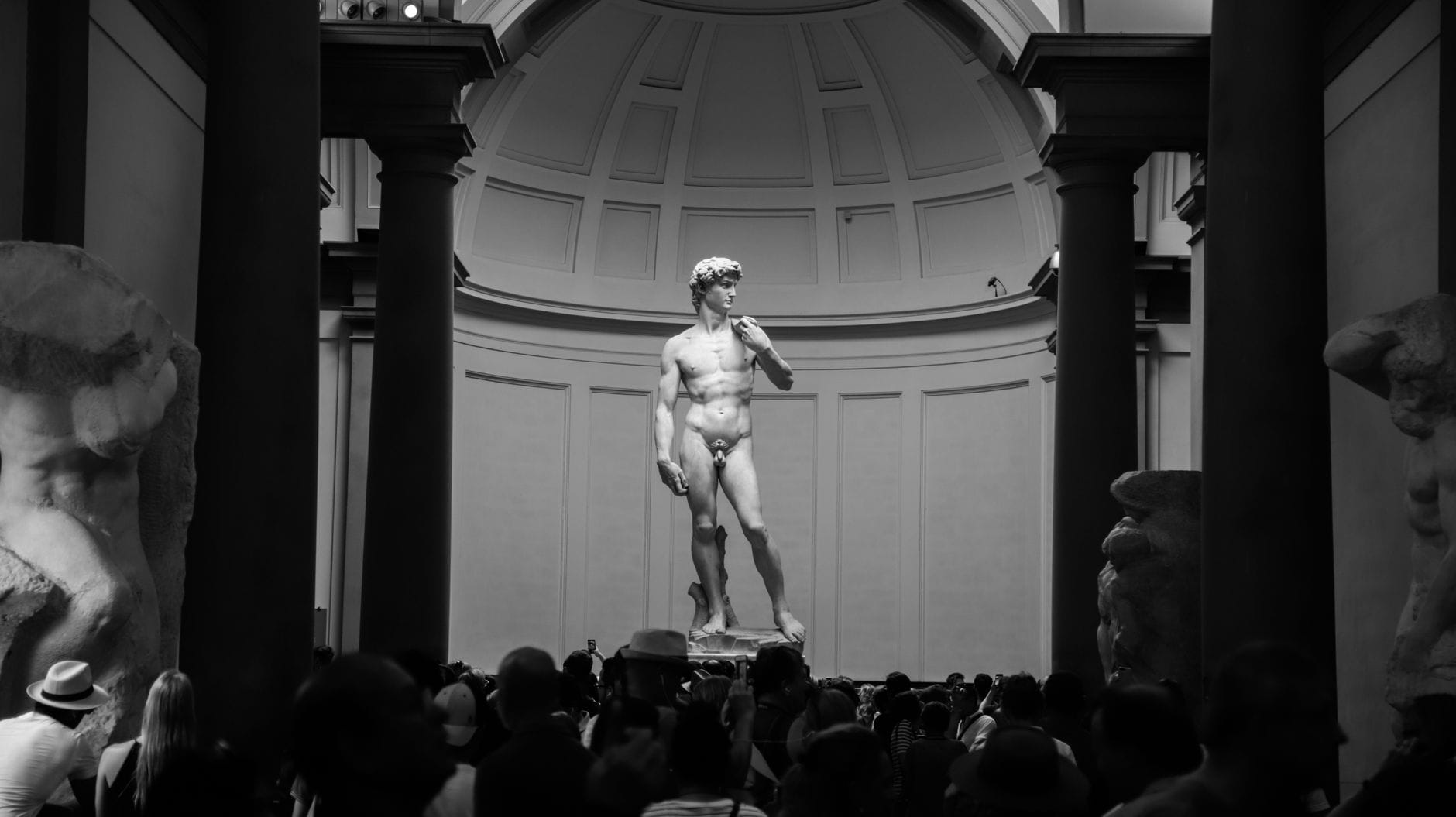 มุมมองกว้างของรูปปั้น David ของ Michelangelo ที่ Galleria dell'Accademia ในเมือง Florence ล้อมรอบด้วยนักท่องเที่ยวและประกอบด้วยประติมากรรม Prisoners ที่ยังสร้างไม่เสร็จอยู่สองข้าง