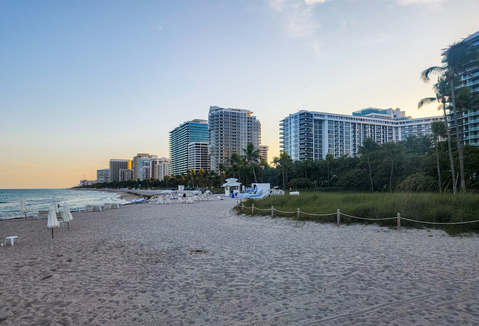 วิวชายหาดทรายกว้าง โรงแรมรีสอร์ททันสมัยเรียงราย มีต้นปาล์มและทะเลใสสงบใต้ท้องฟ้าแจ่มใสที่ไมอามี่บีช