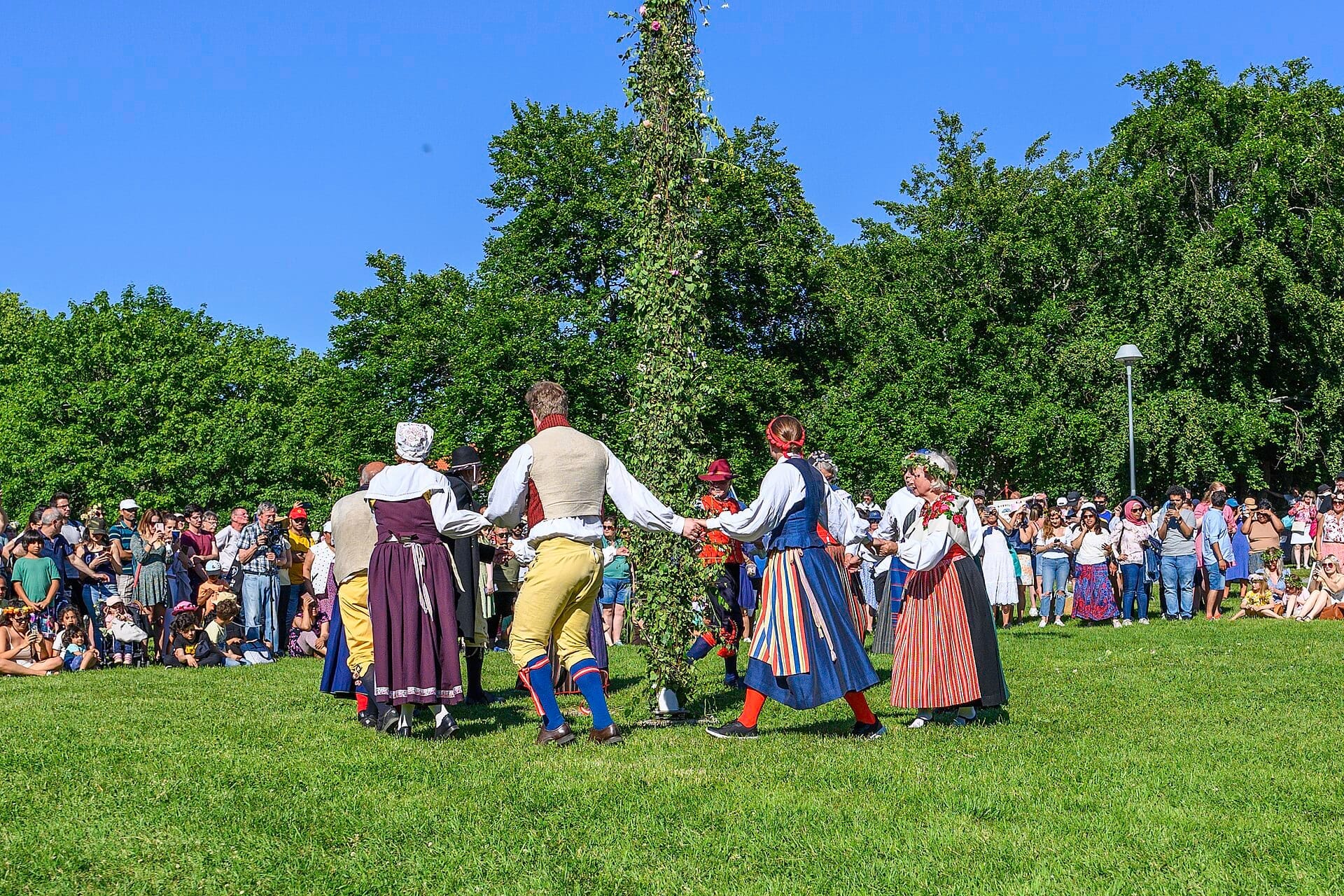 ผู้คนสวมชุดดั้งเดิมของสวีเดนกำลังเต้นรำรอบเสา Maypole ที่ Skansen ในสตอกโฮล์ม ท่ามกลางฝูงชนในวันฤดูร้อนที่แสนแดดจ้า