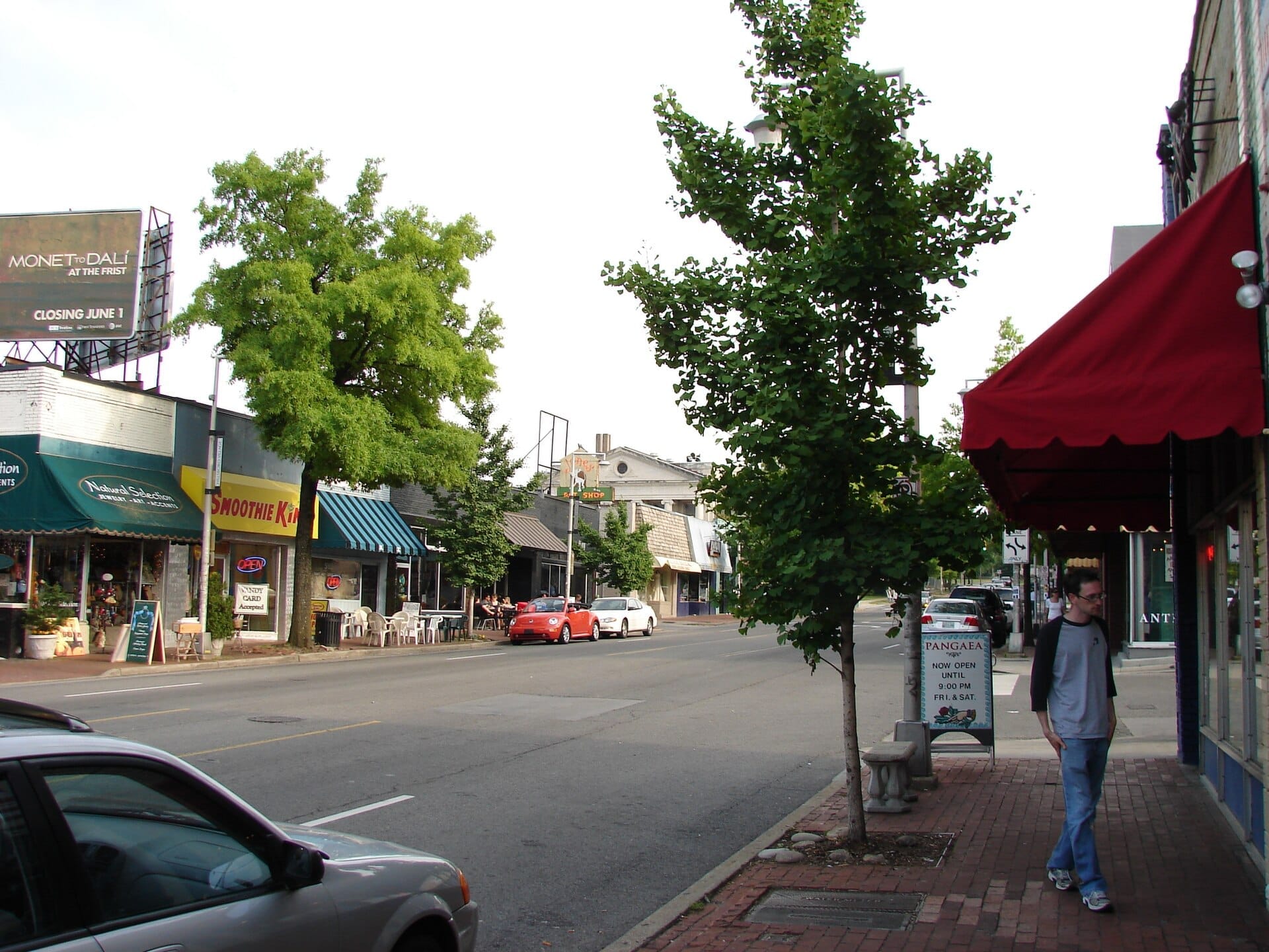 Vista de una calle en Hillsboro Village en Nashville con tiendas locales, una tienda Smoothie King, árboles verdes y algunos autos estacionados en una tarde soleada.
