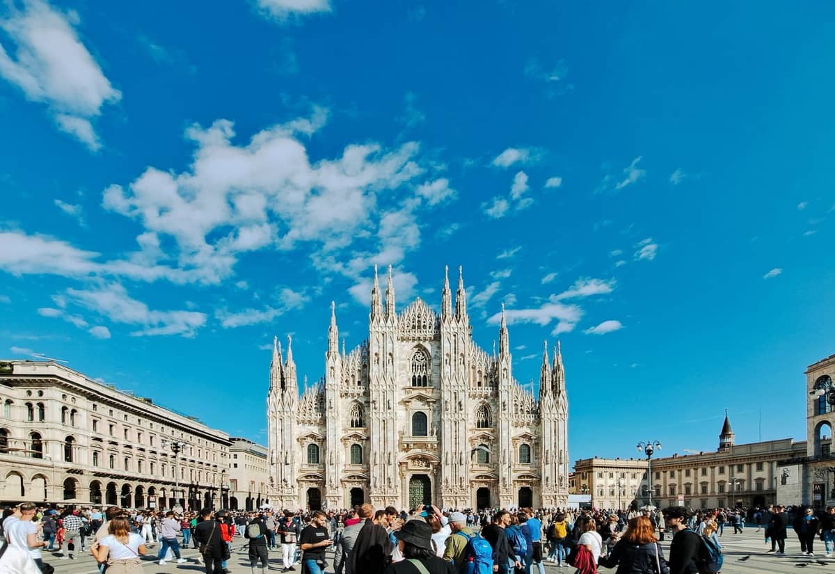 Menschenmassen vor dem Duomo di Milano unter einem blauen Himmel, was auf eine belebte Zeit in der Stadt hindeutet.