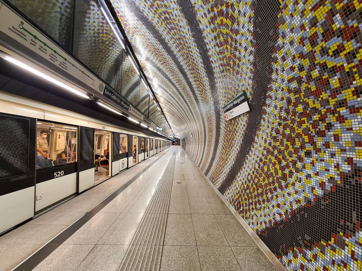 Moderne Mailänder Metro-Station mit markanter Mosaikwand und einfahrendem M4-Zug auf dem Bahnsteig.