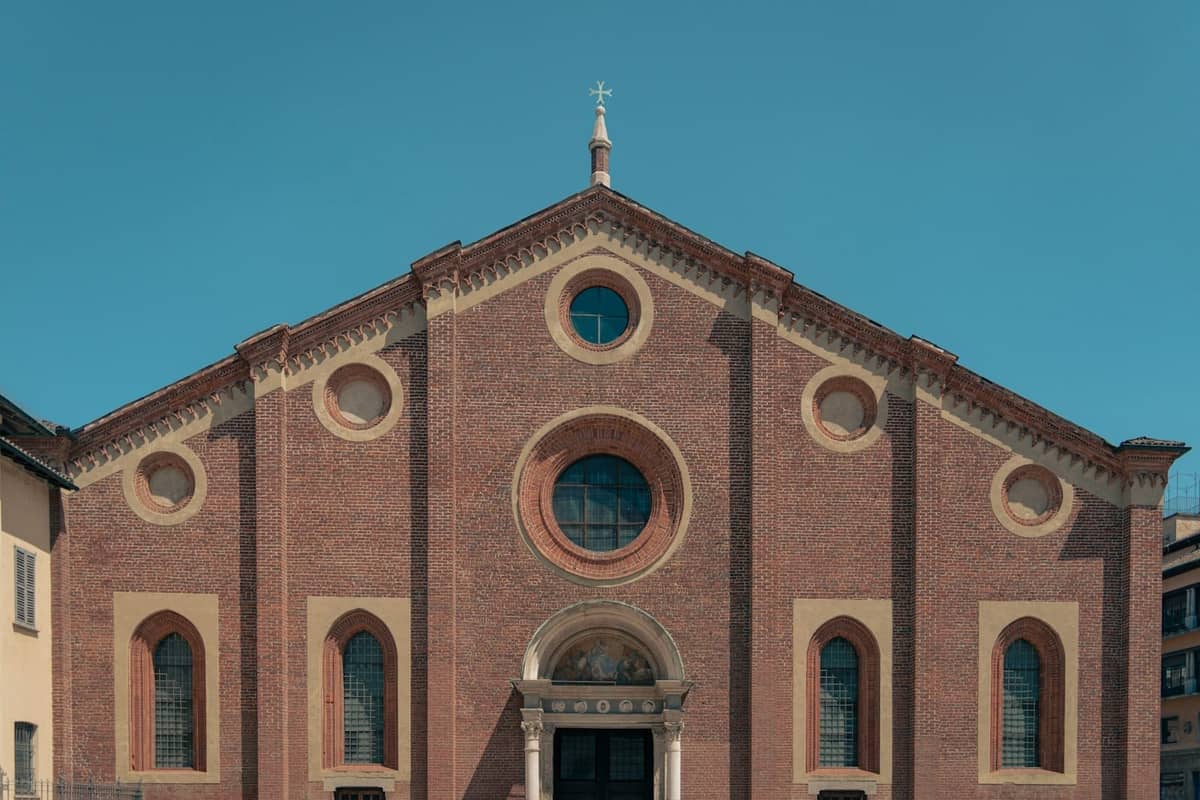 Facciata di Santa Maria delle Grazie a Milano, una chiesa rinascimentale in mattoni rossi con archi decorativi sotto un cielo sereno.
