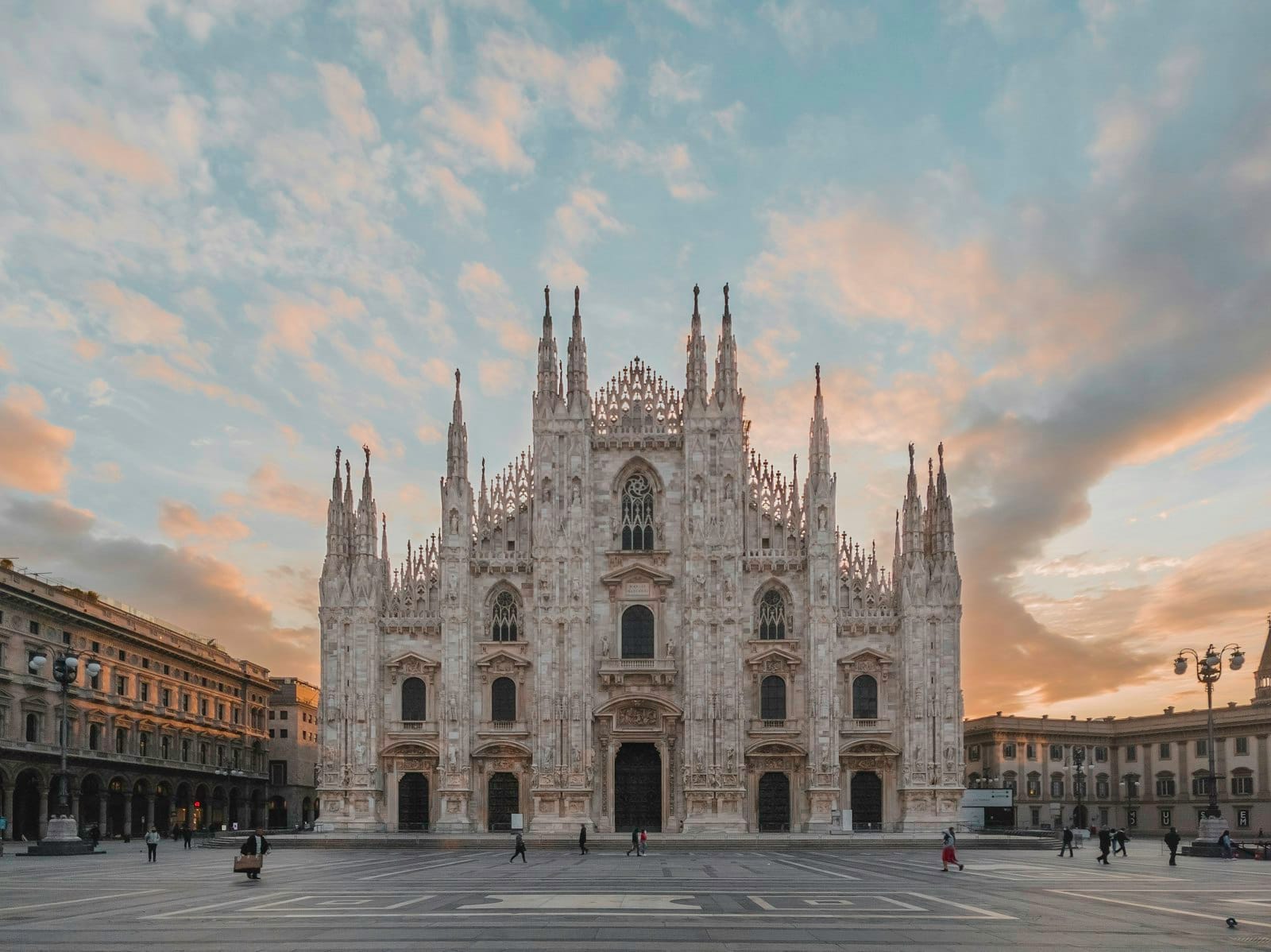 Vista frontal da Catedral de Milão (Duomo di Milano) ao amanhecer com céu dramático, praça principal vazia e linda arquitetura gótica.
