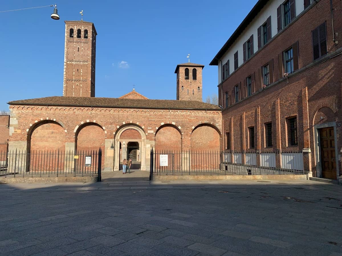 Sonnenbeschienene Ansicht der antiken Basilica di Sant'Ambrogio in Mailand mit ihrer romanischen Backsteinfassade, dem Bogendurchgang und zwei mittelalterlichen Türmen.