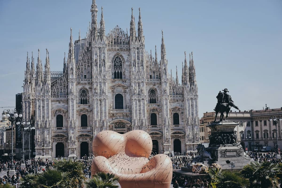 Piazza del Duomo a Milano con una grande installazione d'arte moderna in primo piano durante un affollato evento pubblico.