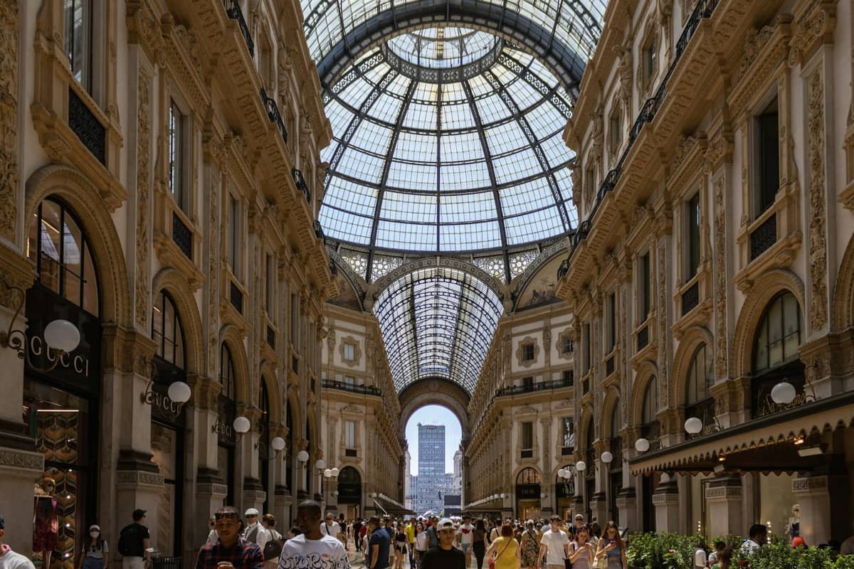 Die elegante, glasüberdachte Galleria Vittorio Emanuele II in Mailand, gefüllt mit Menschen und gehobenen Geschäften wie Gucci, die Mailands Ruf als globale Modemetropole verkörpert.