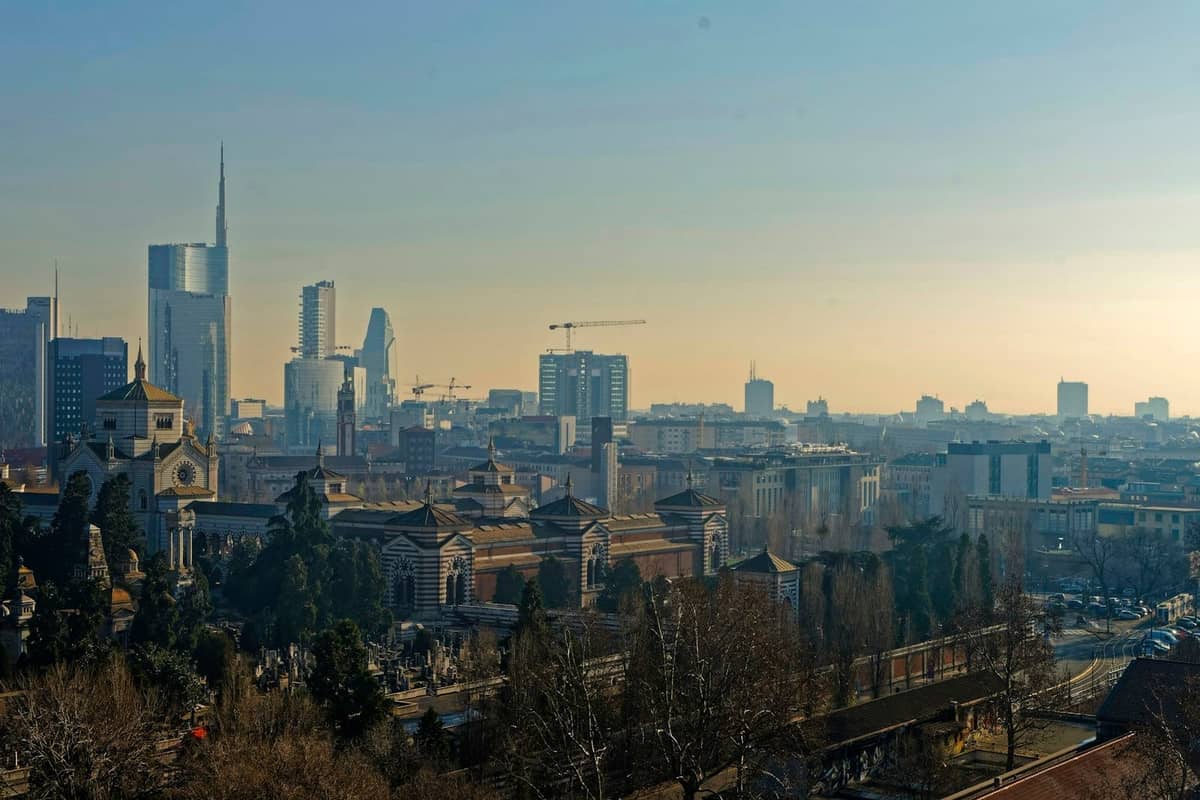 Luftaufnahme von Mailand mit Grünflächen, den Mauern des Castello Sforzesco und modernen Wolkenkratzern in der Ferne unter klarem Himmel.