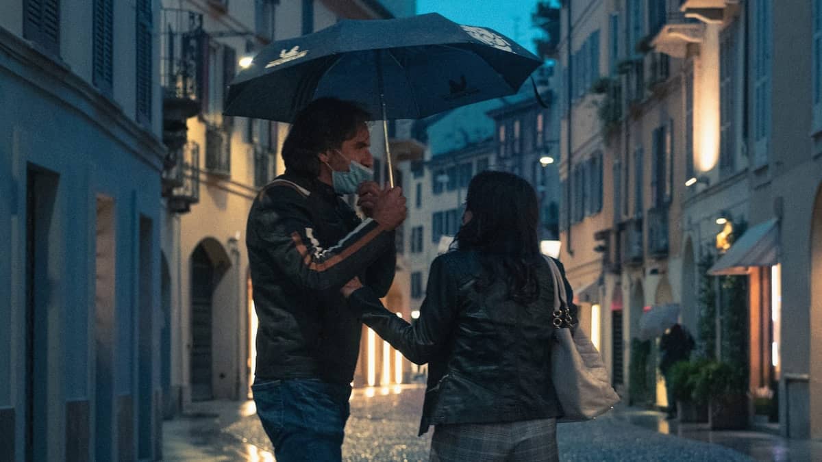 Pärchen unter einem Regenschirm, das in der Abenddämmerung durch eine bezaubernde Straße in Mailand spaziert, umgeben von sanft beleuchteten historischen Gebäuden.