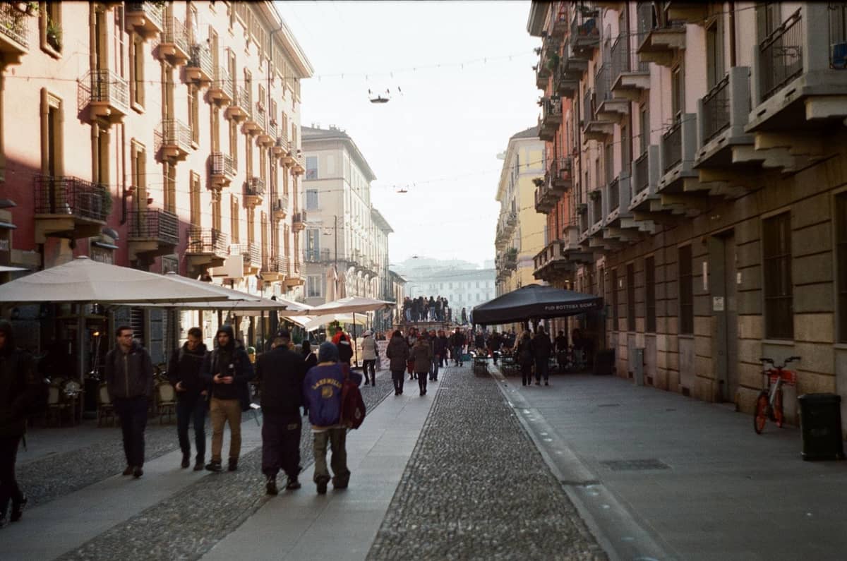 Enge Kopfsteinpflasterstraße in Mailand, gesäumt von historischen Gebäuden, Straßencafés und Menschen, die an einem sonnigen Tag schlendern.