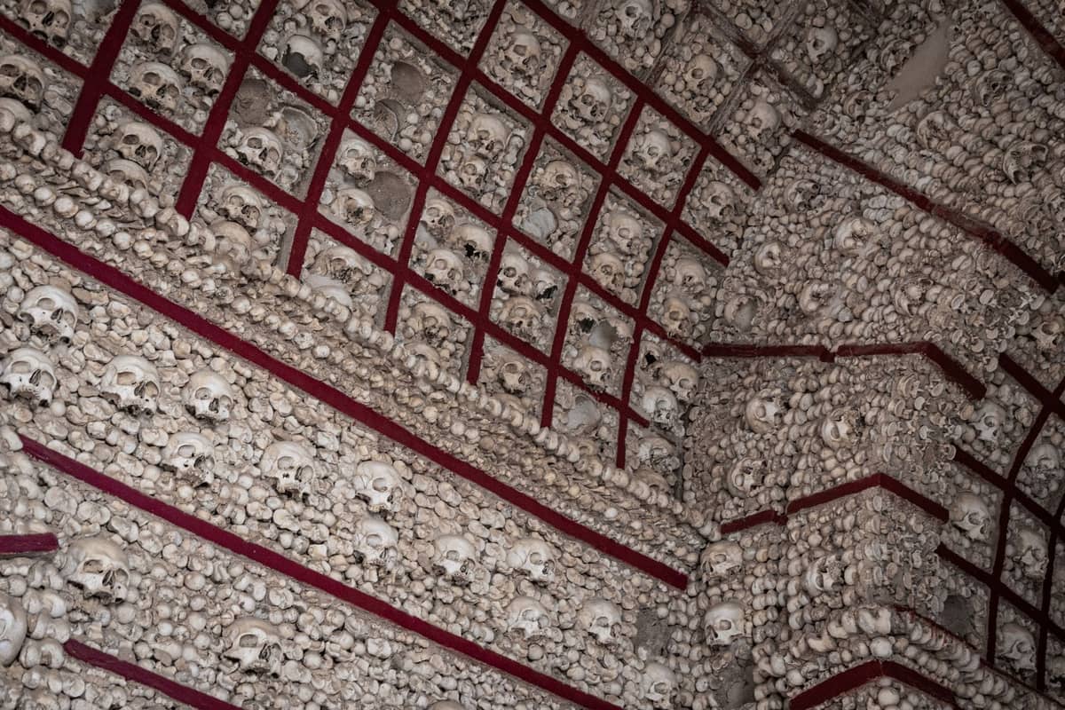 Wand aus menschlichen Schädeln und Knochen in einem geometrischen Rastermuster, das auf ein historisches Ossarium oder eine Krypta hindeutet.