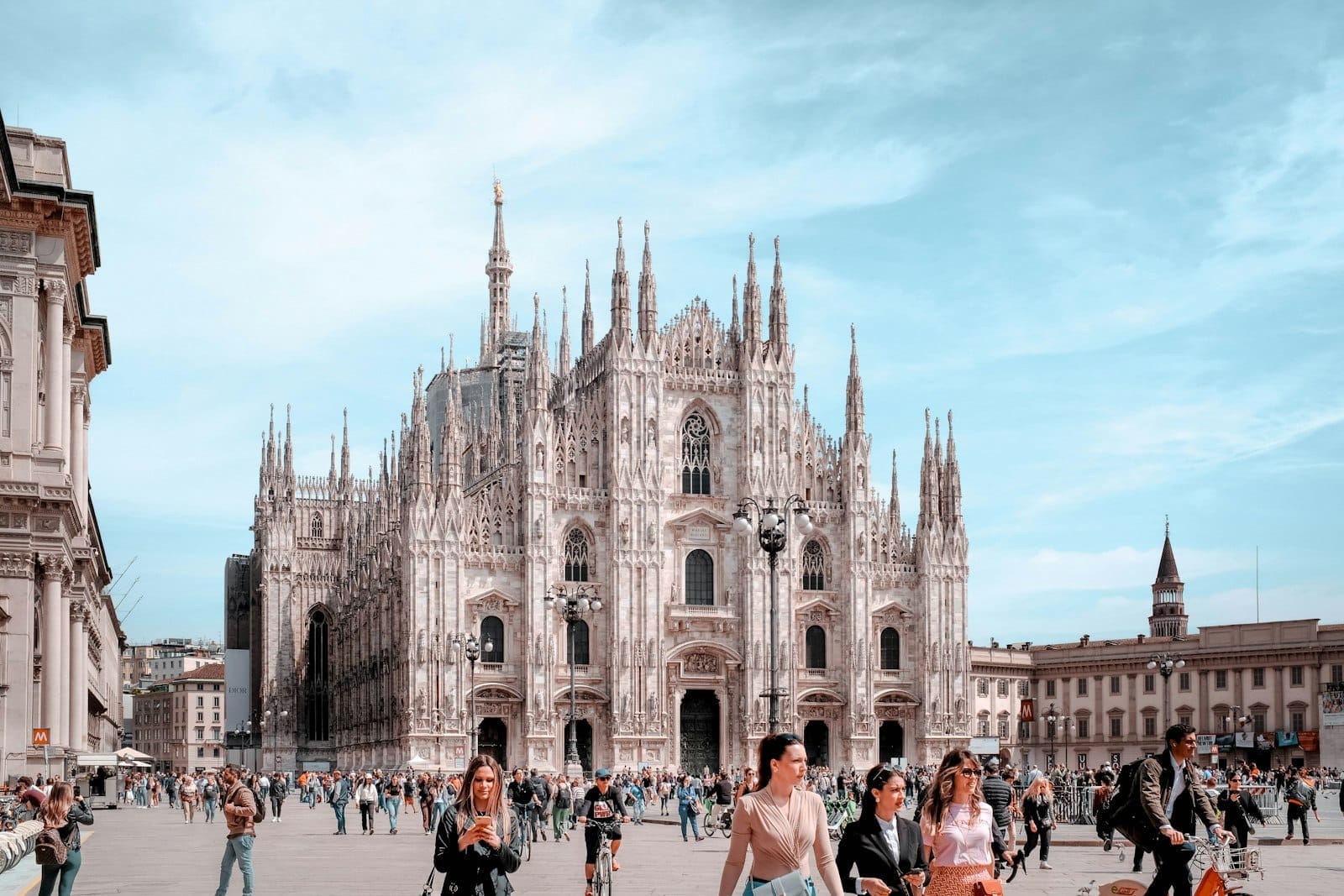 Pessoas caminhando na Piazza del Duomo em um dia ensolarado de primavera com a Catedral de Milão ao fundo sob um céu azul.