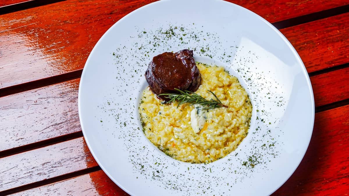 Teller mit Safranrisotto und geschmortem Fleisch, garniert mit frischen Kräutern auf einem Holztisch in einem Restaurant.