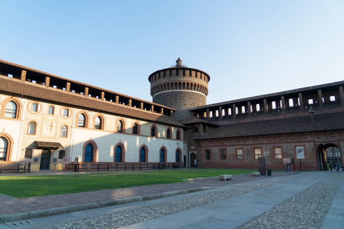 Innenhofansicht des Castello Sforzesco in Mailand mit dem ikonischen Rundturm unter klarem blauem Himmel, während Sonnenlicht die Burgmauern beleuchtet.