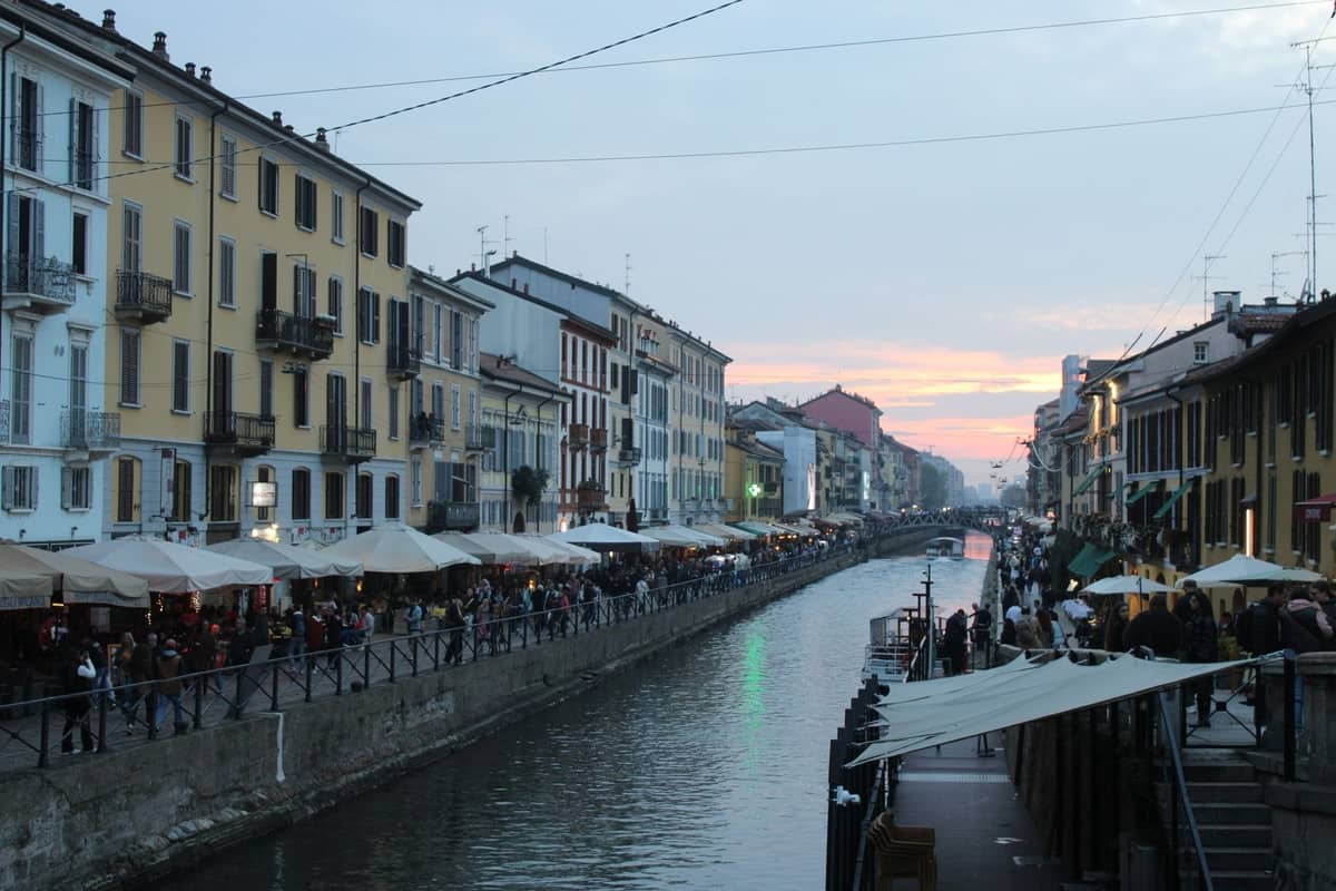 Belebte Kanalstraße bei Sonnenuntergang im Navigli-Viertel von Mailand mit lebhaften Bars und Menschen, die den Abend genießen.