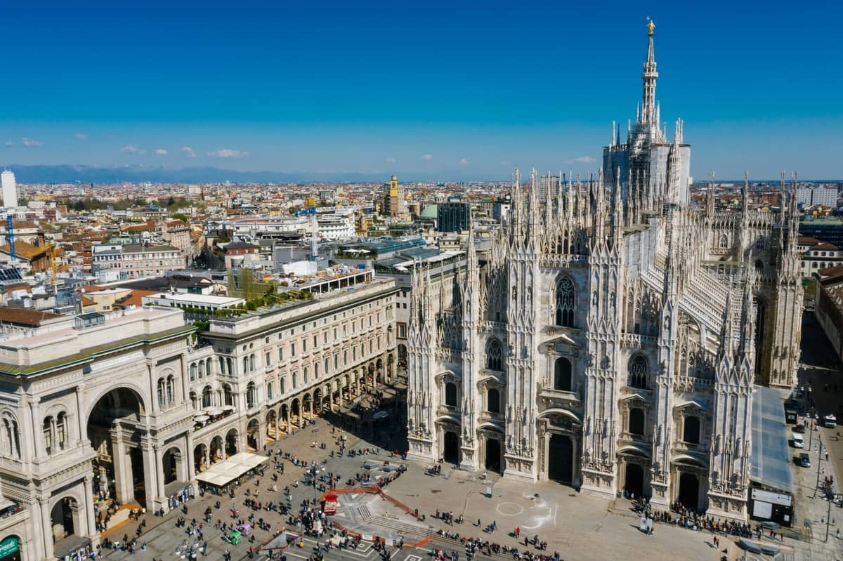 Toàn cảnh nhìn từ trên cao của nhà thờ Duomo mang tính biểu tượng của Milan và thành phố xung quanh với bầu trời quang đãng và quảng trường piazza nhộn nhịp bên dưới.
